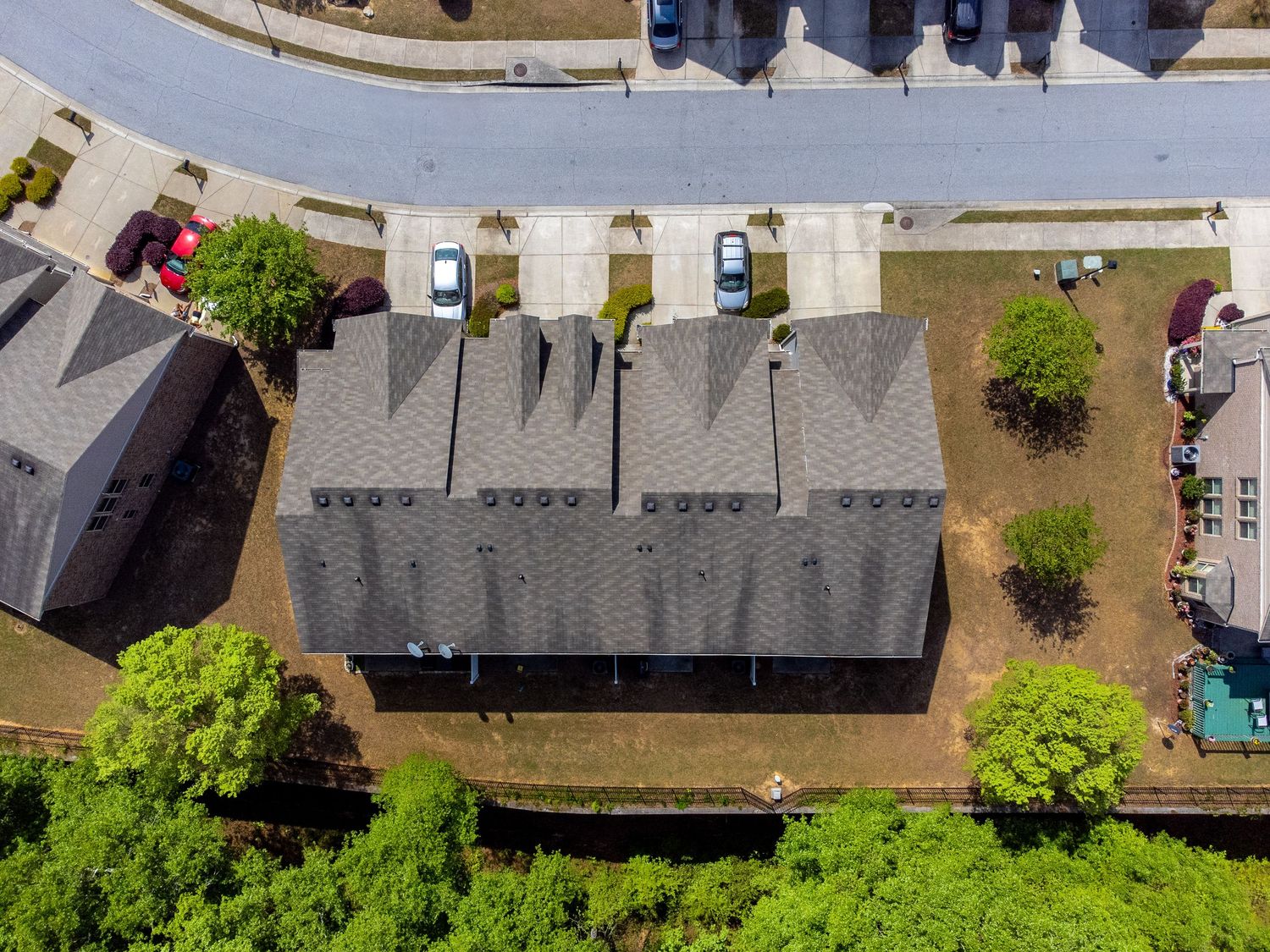 Aerial view of residential neighborhood with asphalt roofs, driveways, and green trees on a sunny day.
