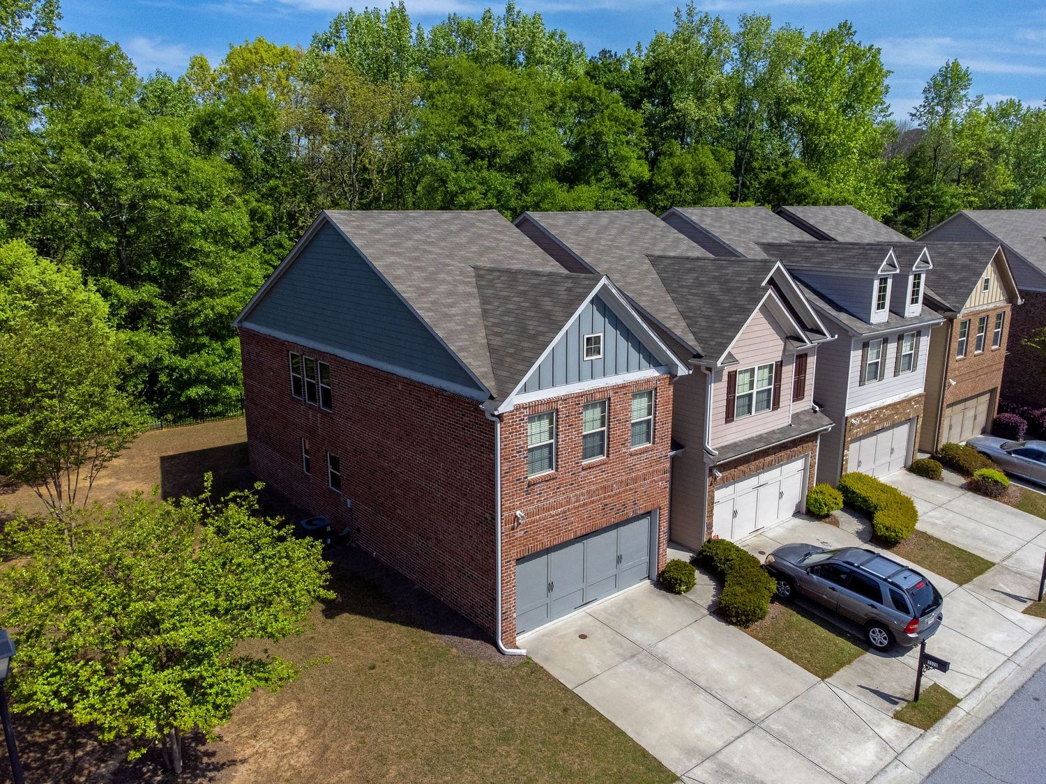 Aerial drone view of suburban homes with driveways and green trees in a residential neighborhood on a sunny day.