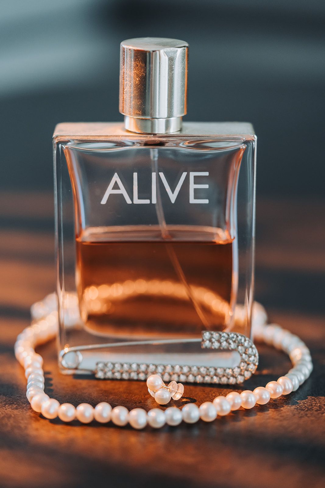 Perfume bottle labeled 'ALIVE' with pearl necklace on wooden surface.