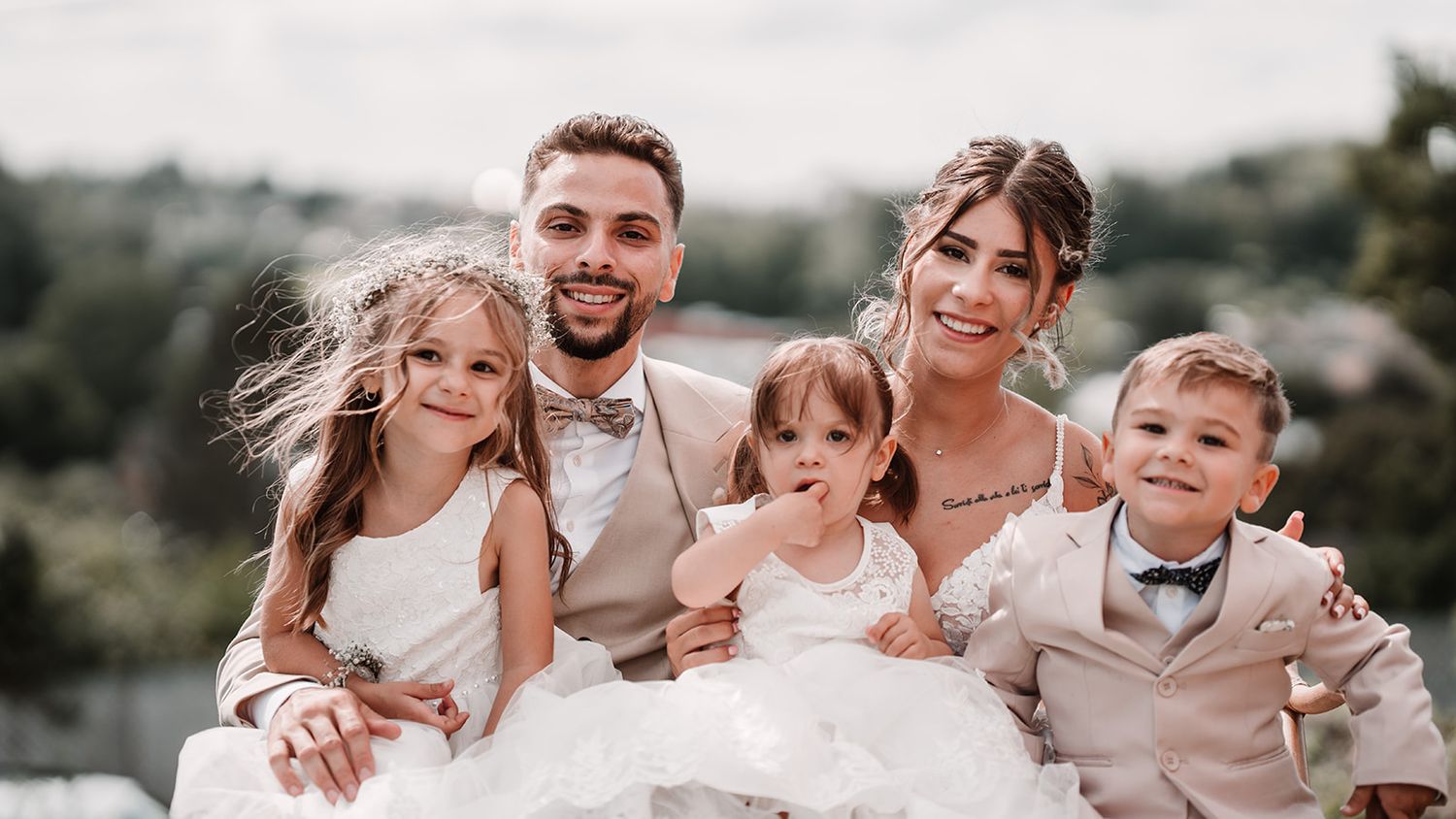 Wedding party members embrace and laugh together outdoors in coordinated outfits.