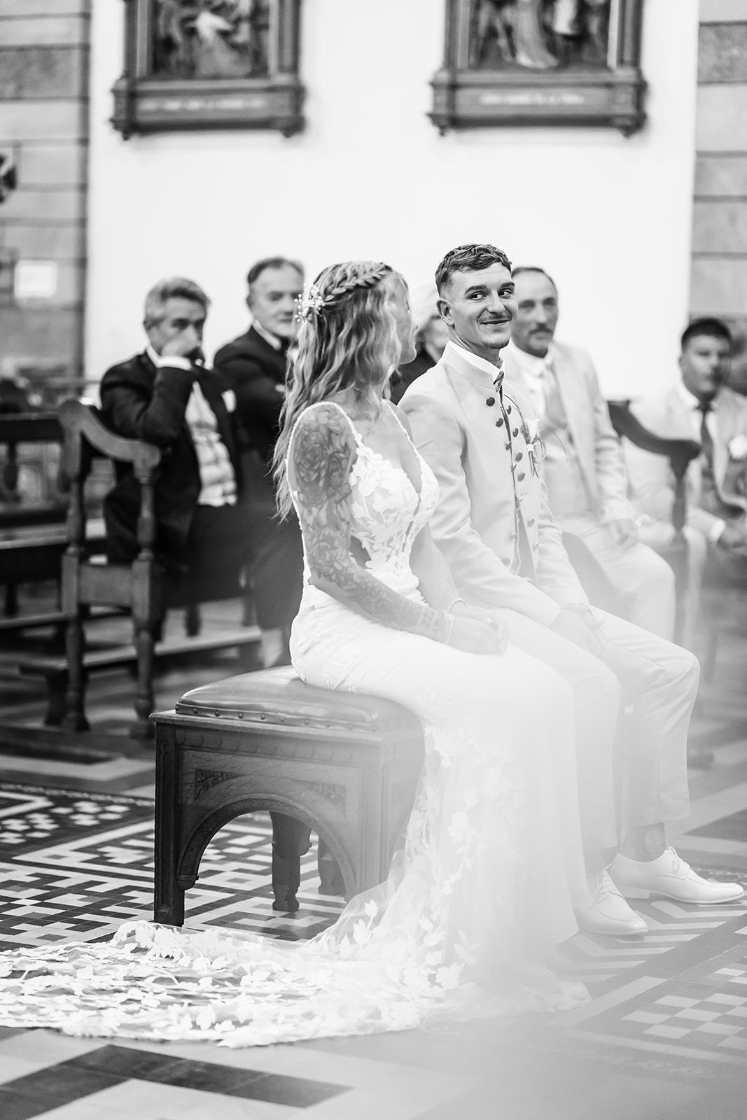 Black and white photo of a couple sitting during their wedding ceremony in a church.