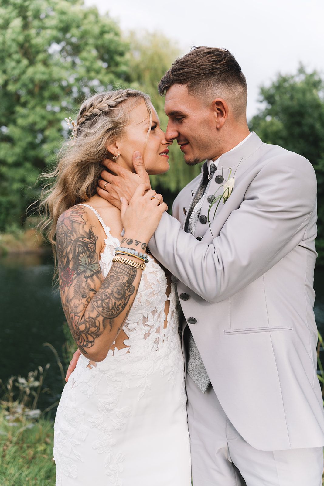 Newlyweds share an intimate moment outdoors, with the bride showing off intricate arm tattoos in her lace dress.