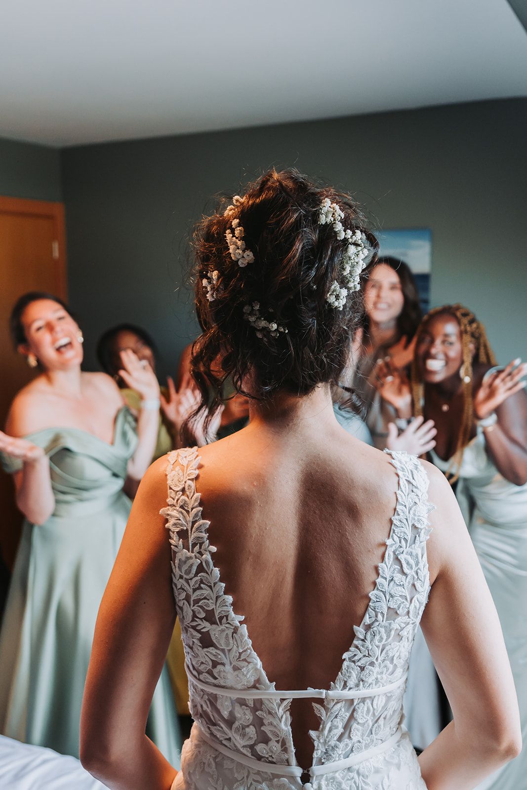 Back view of a bride in lace dress with bridesmaids reacting in background.