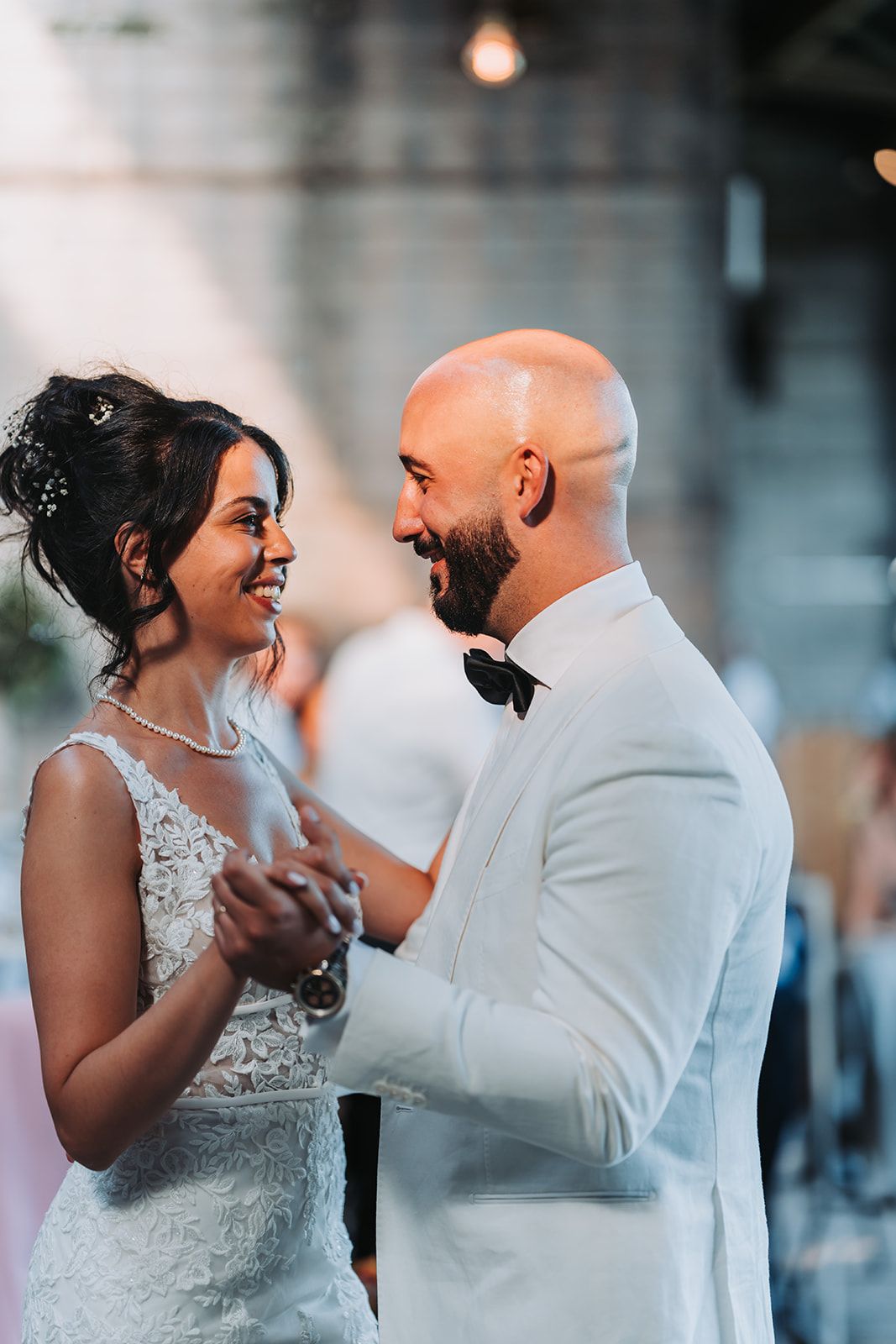 A joyful couple shares an intimate dance moment at their wedding reception in white attire.