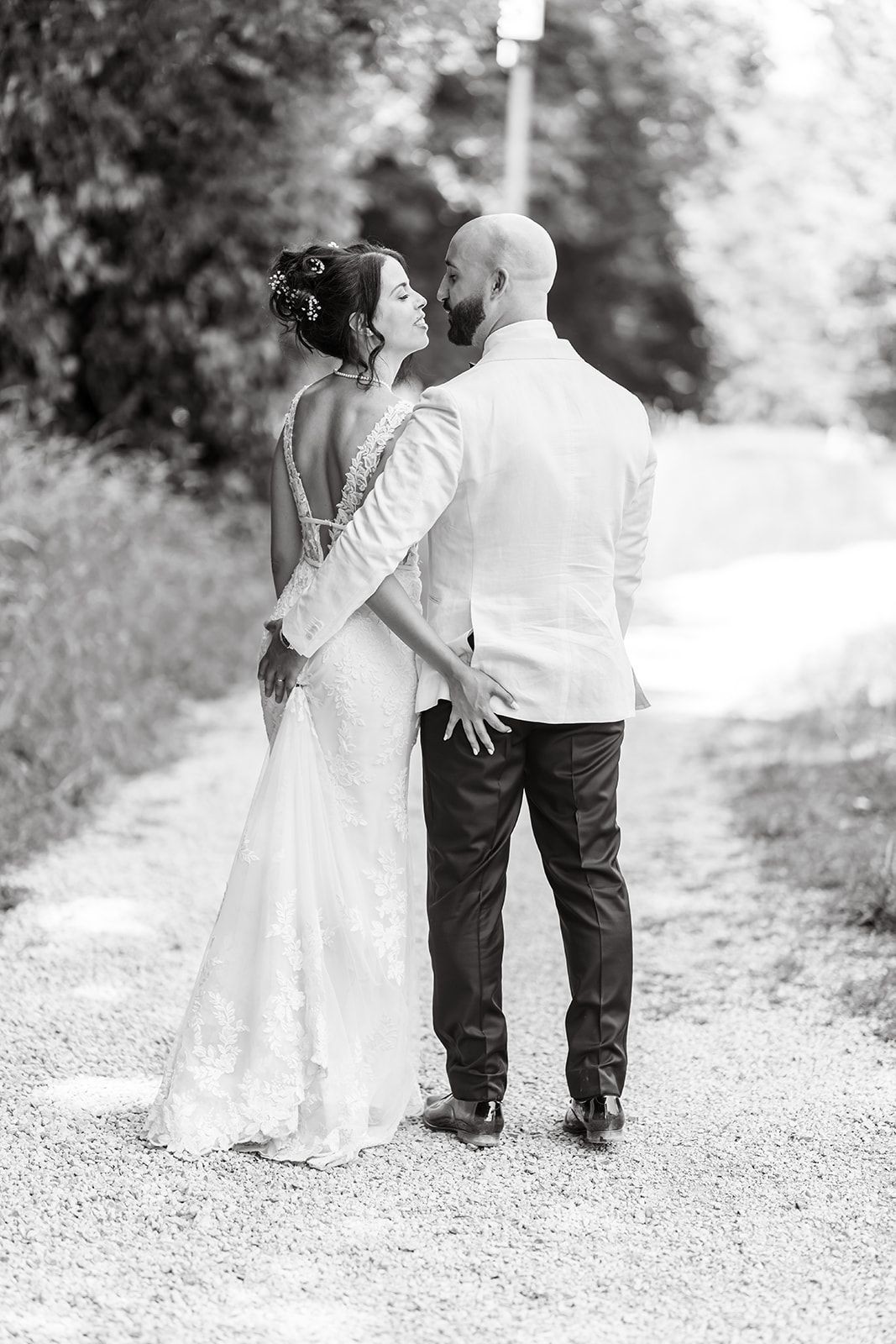 A romantic black and white wedding photo showing a couple embracing on a tree-lined path.