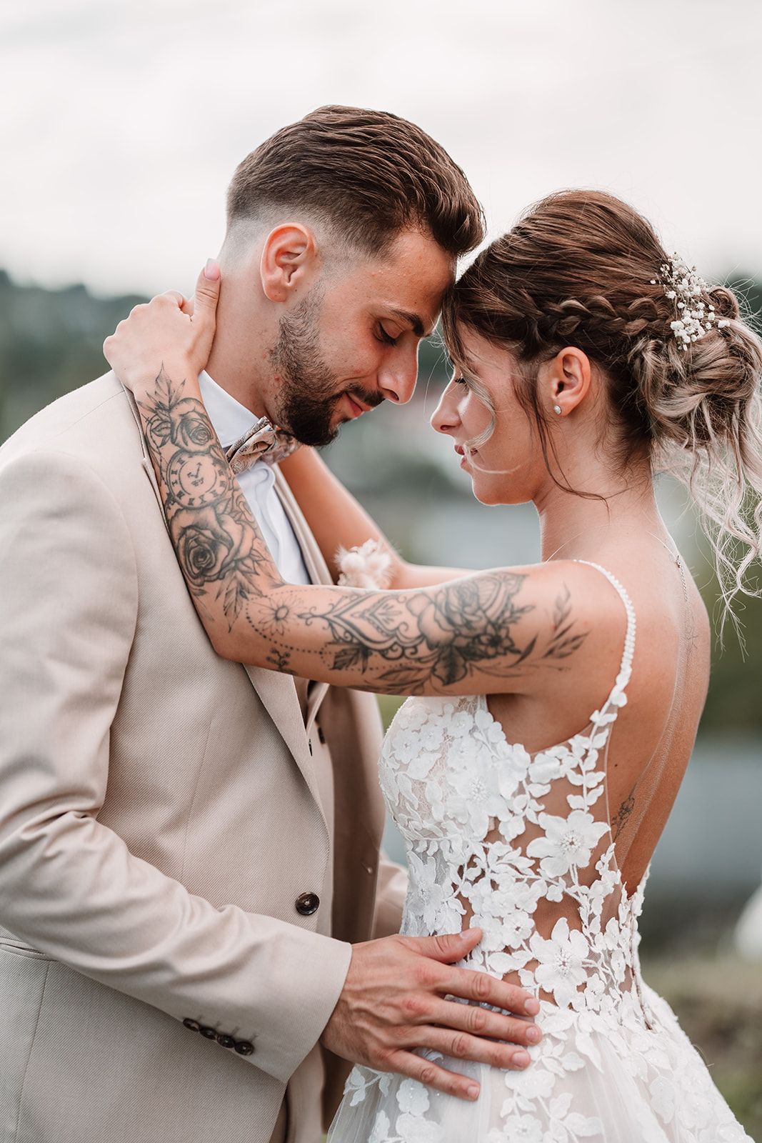 Romantic wedding couple shares intimate moment in beige and white attire with visible tattoos.