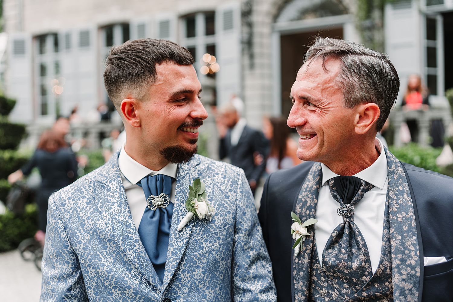 Two men in formal attire share joyful moment at outdoor wedding celebration.
