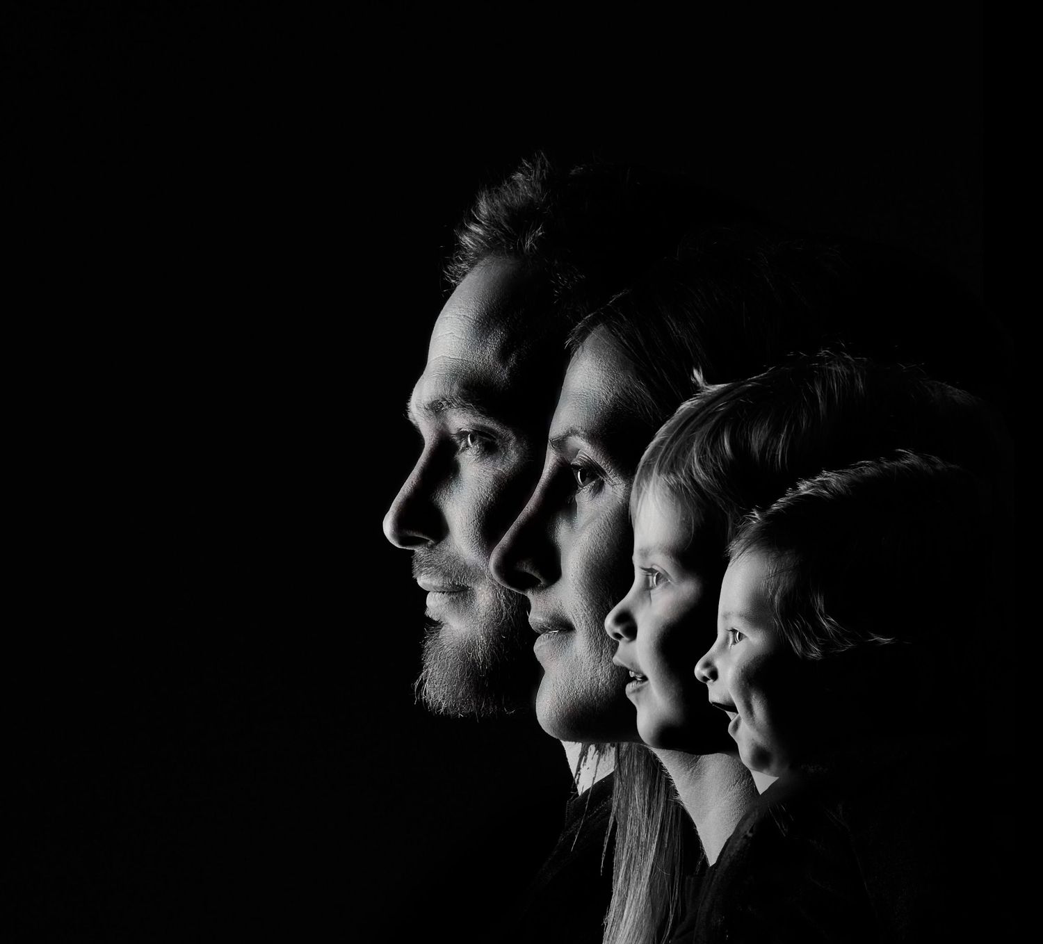 Black and white family portrait of four people in profile against dark background.