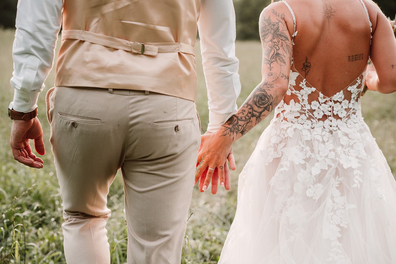 Close-up of wedding couple showing detailed lace dress and tan suit from behind.