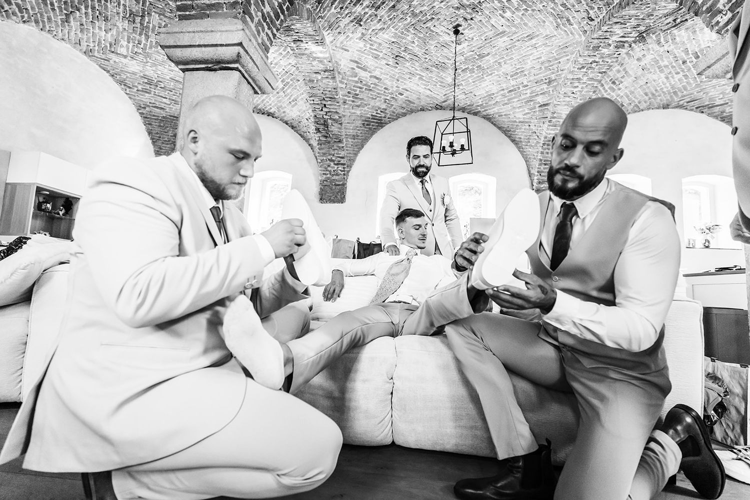 Black and white photo of groomsmen sharing drinks in an elegant arched venue.