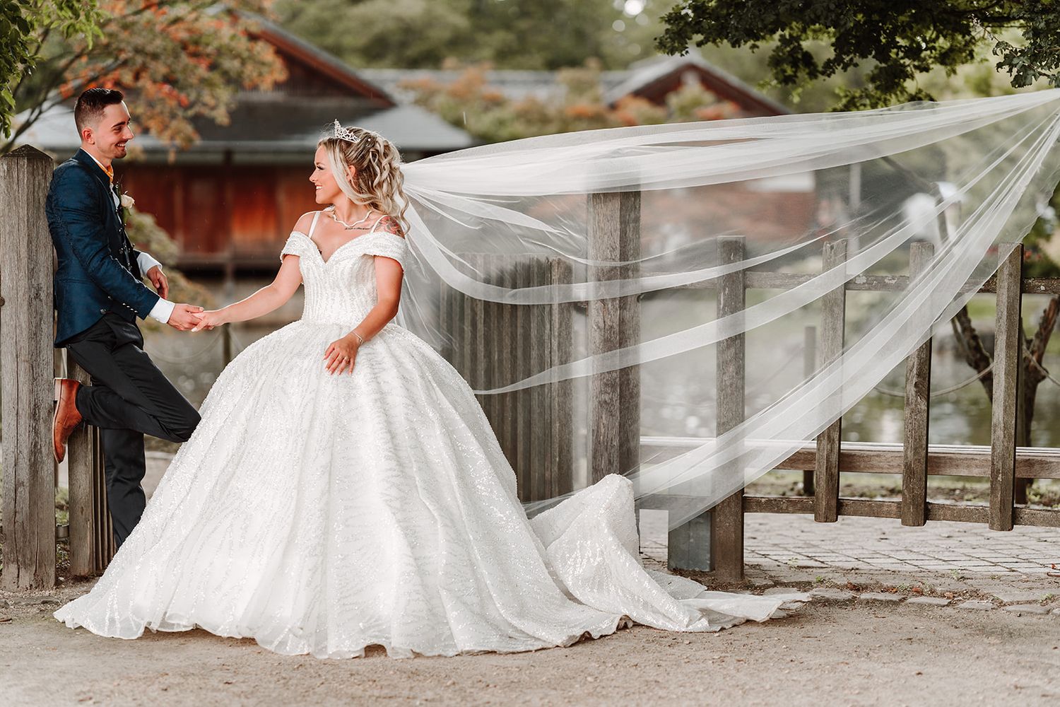 Long bridal veil flows dramatically across outdoor garden setting.