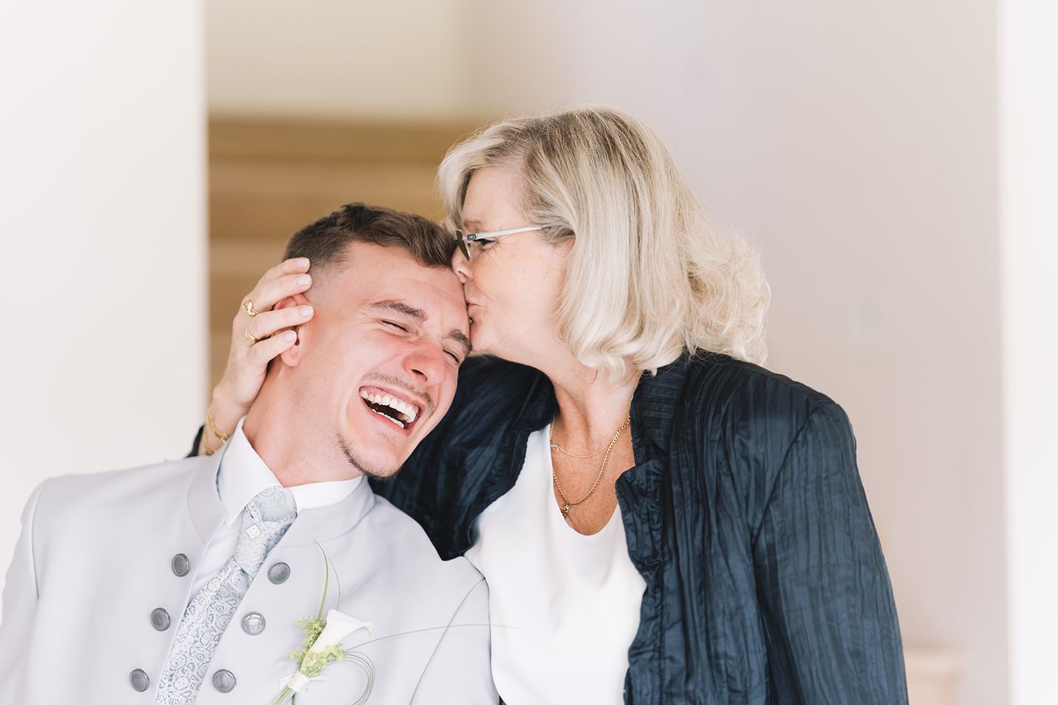 Moment d'émotion entre un marié et sa mère, tendresse et rires pendant la journée de mariage.