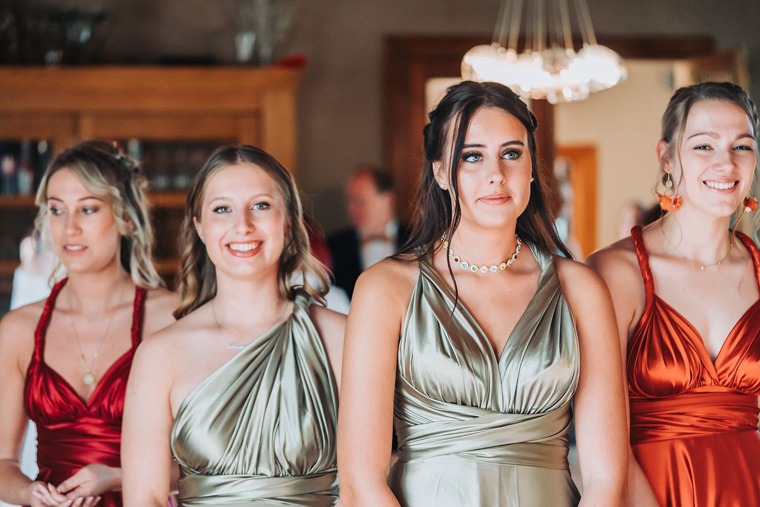 Bridesmaids wearing mix of metallic and burgundy satin dresses pose together.