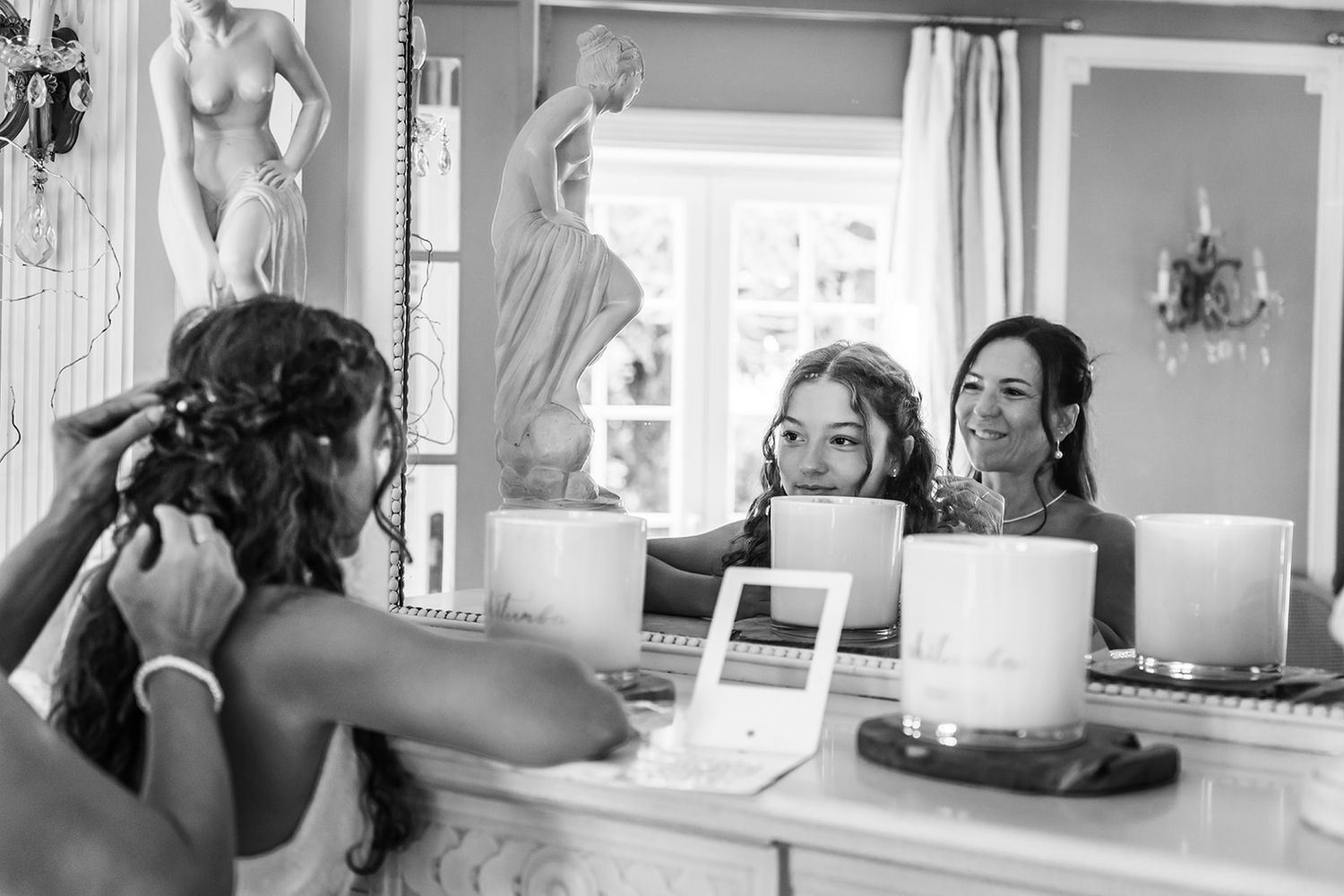 Mise en beauté de la mariée vue à travers un miroir, photographie de mariage artistique en noir et blanc.
