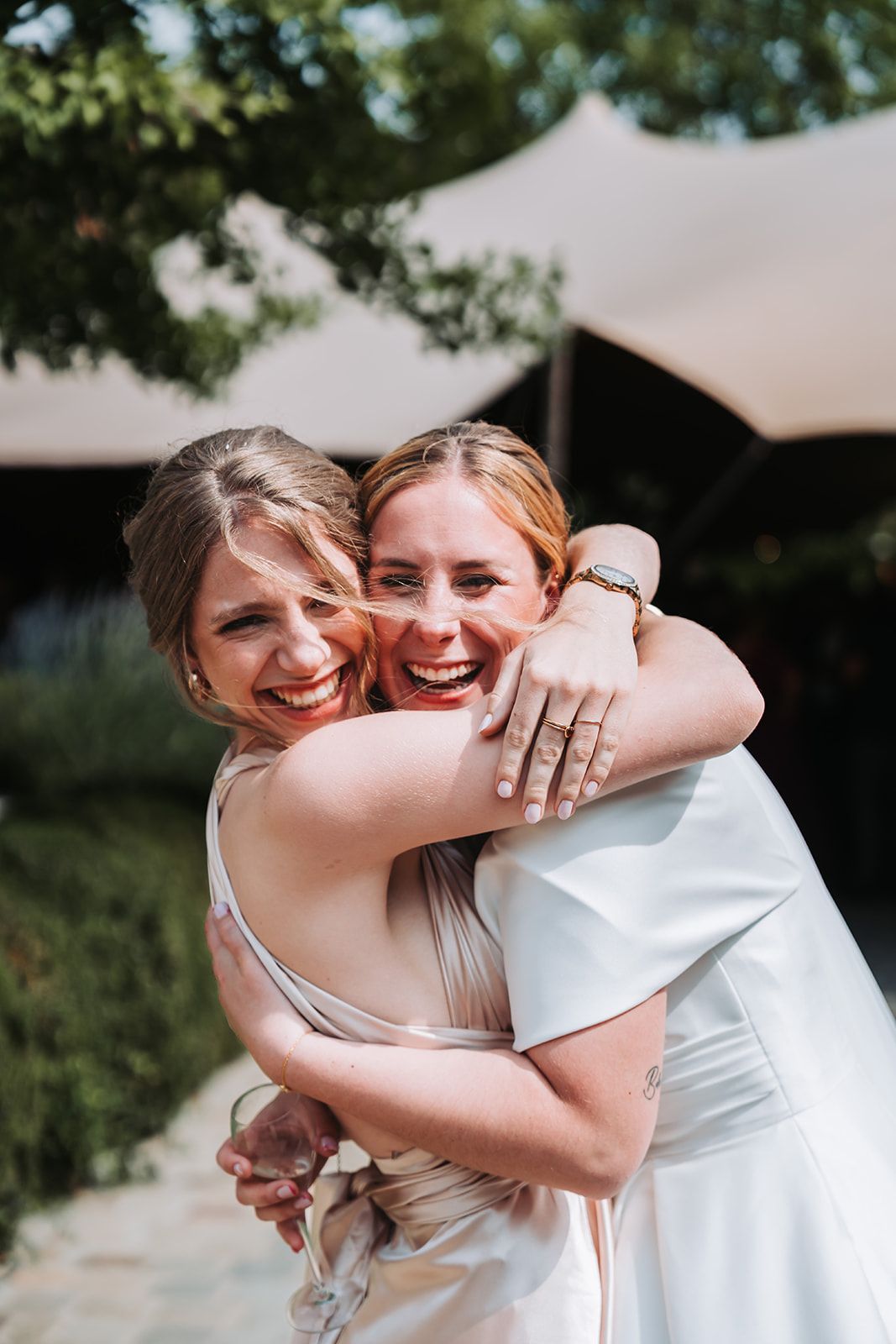 Joyful embrace between wedding party members in outdoor garden setting.
