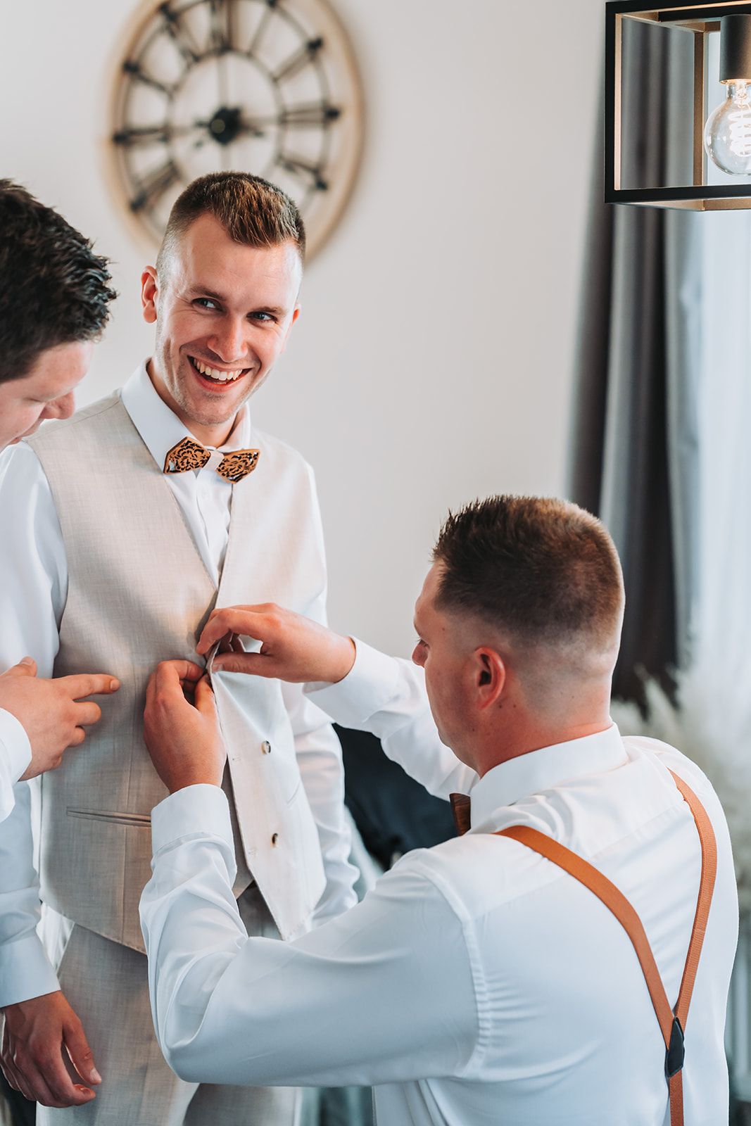 Groomsmen assist with bow tie and formal wear preparations before ceremony.