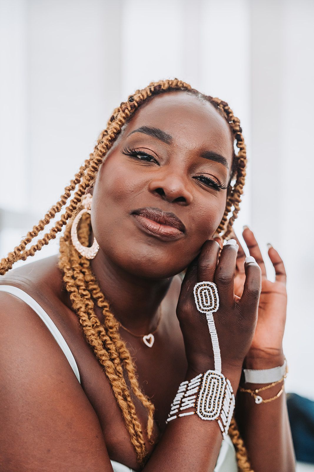 Portrait of a woman with caramel braids wearing statement jewelry and a white tank top.