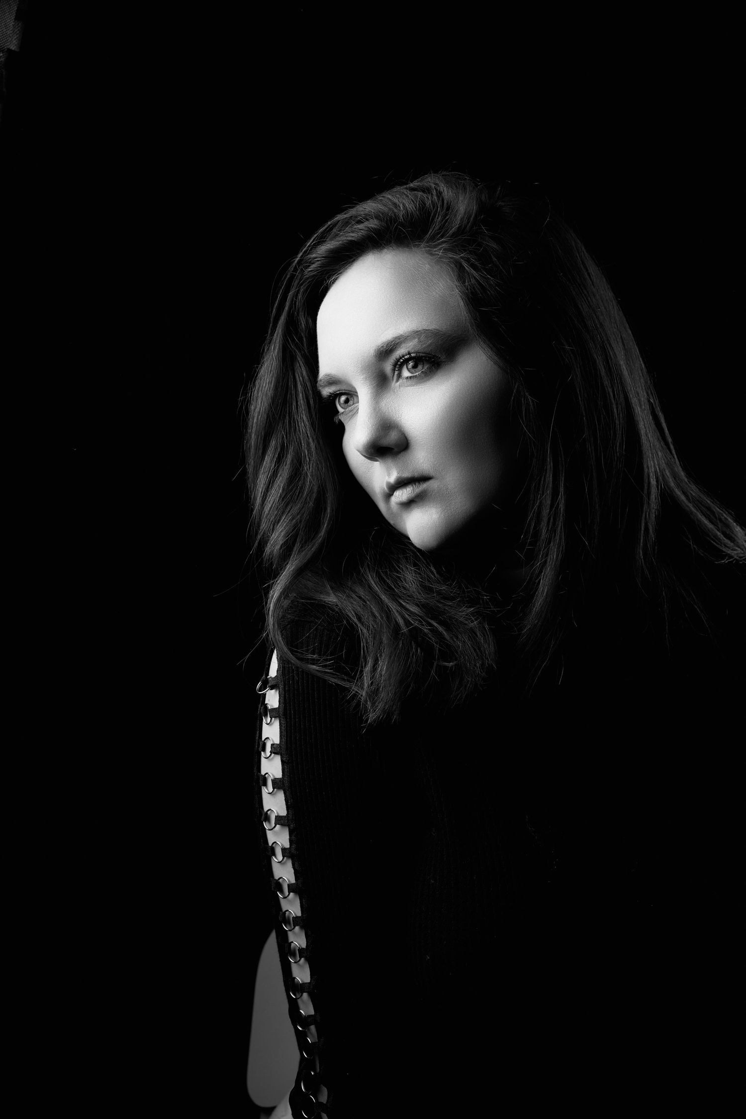 Black and white portrait of a young woman with long dark hair against a dark background, dramatic lighting.
