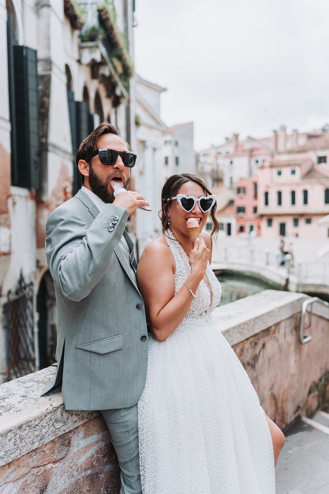 Couple in wedding attire eating ice cream on a bridge in Venice.