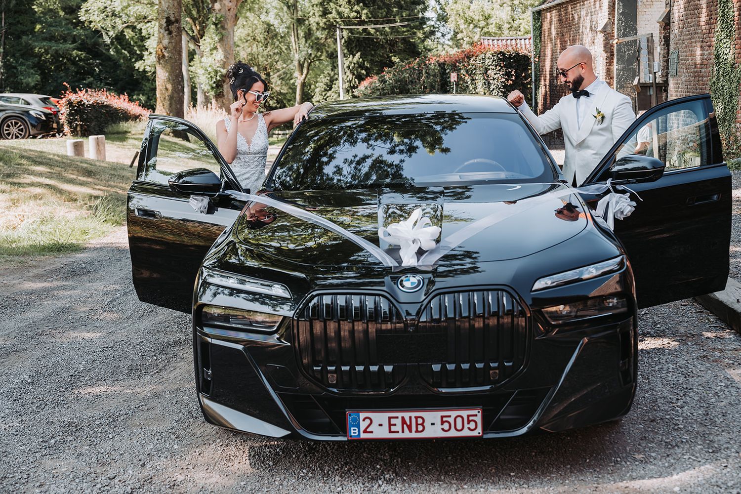 Newlyweds pose with a sleek black luxury car decorated with wedding ribbons.