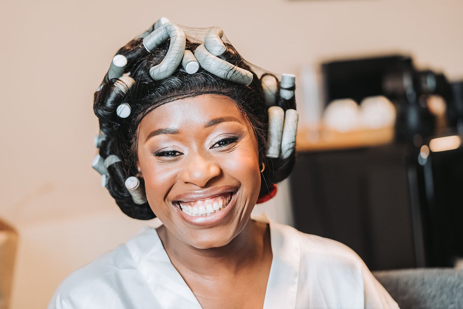 Portrait d'une mariée souriante durant sa séance coiffure et maquillage, moment de complicité.