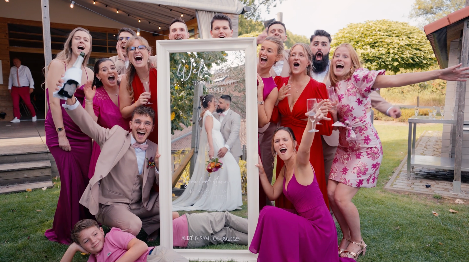 Animation mariage originale : invités posant avec un cadre photo doré dans un jardin, photographe mariage Brabant Wallon.