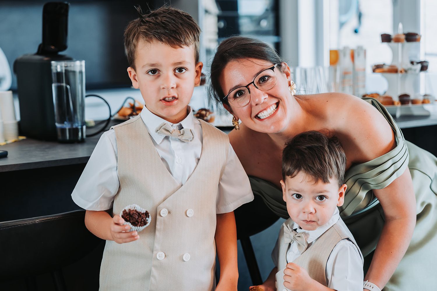 Candid family moment in a kitchen with two young boys in matching beige suits.