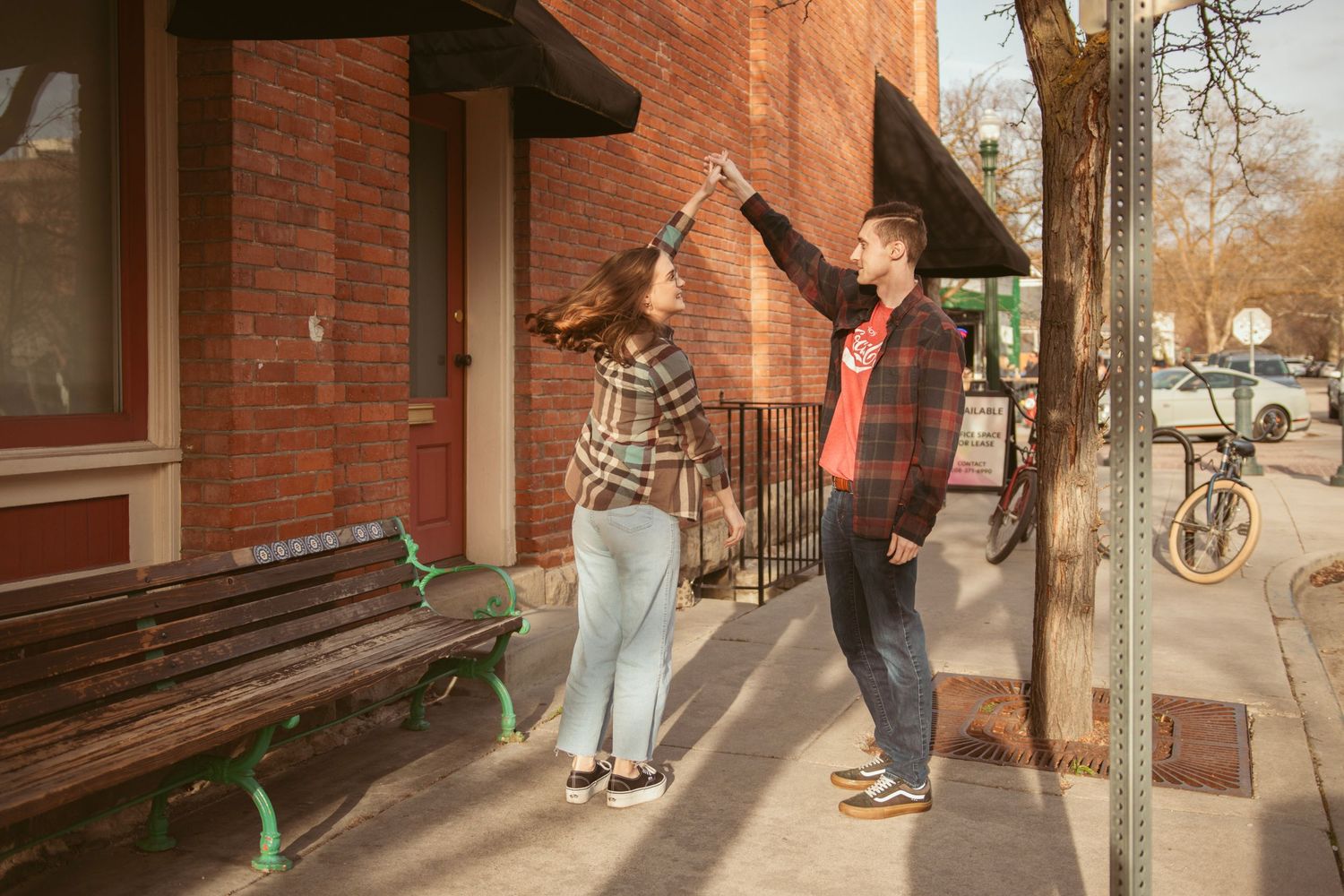 Two people reach up in a synchronized dance pose outside a brick storefront.