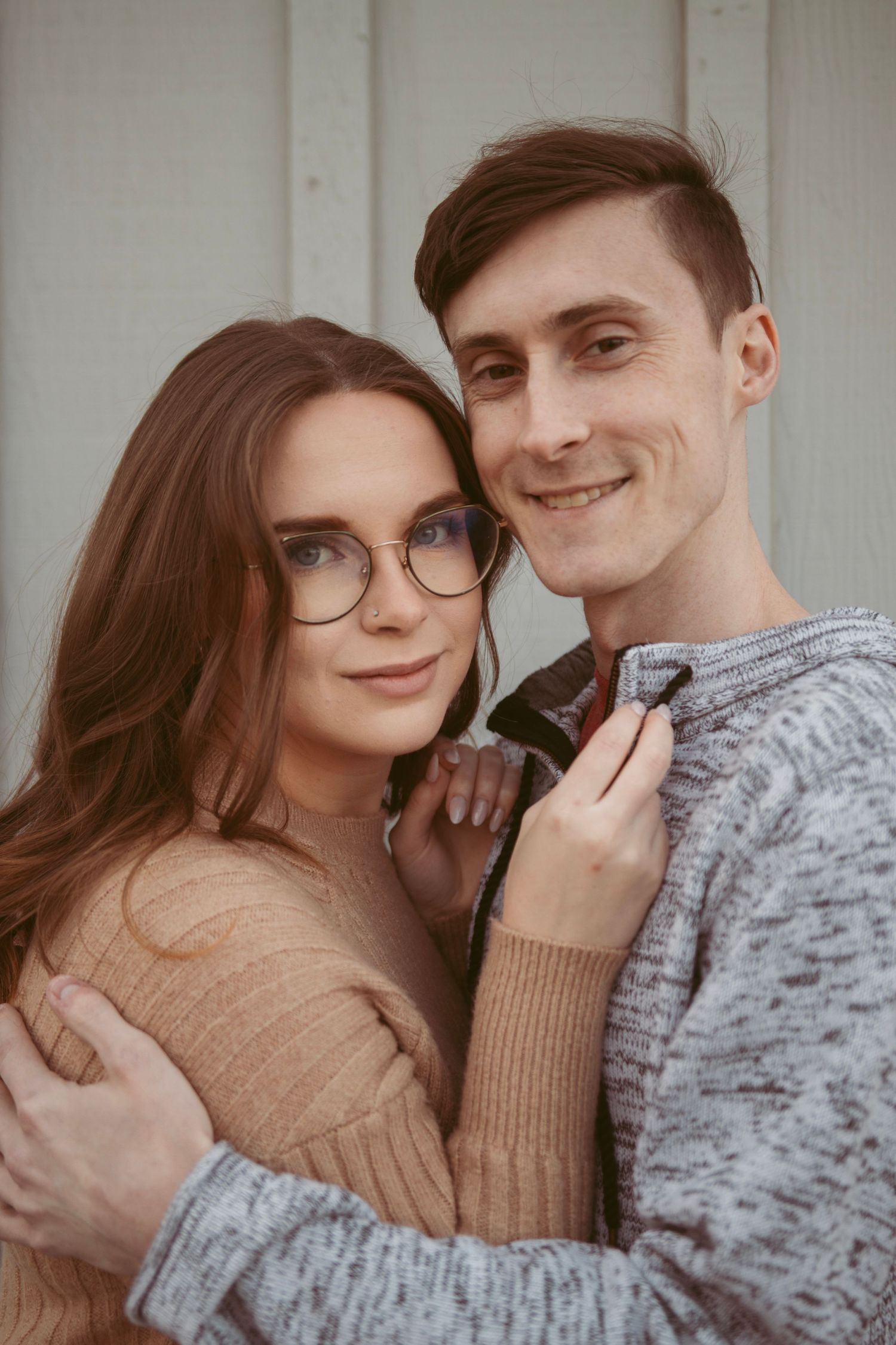 A couple embraces while wearing winter clothing against a light background.