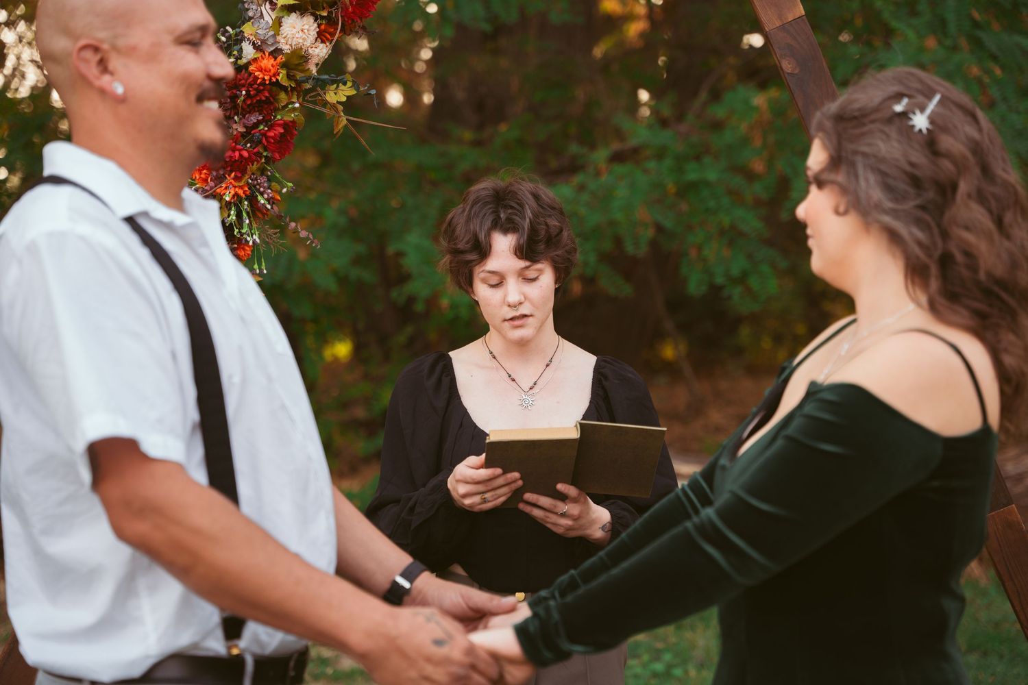Wedding party members interacting during an outdoor ceremony with natural woodland backdrop.