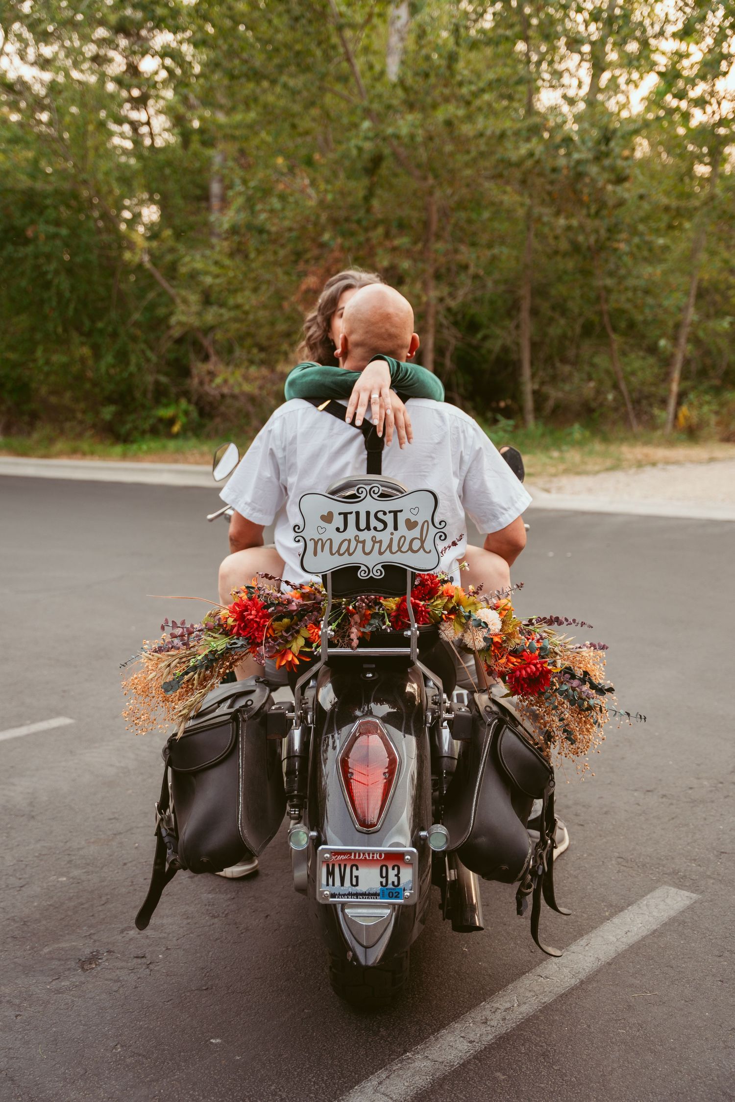 A motorcycle decorated with floral arrangements and a 'Just Married' sign parked in a lot.