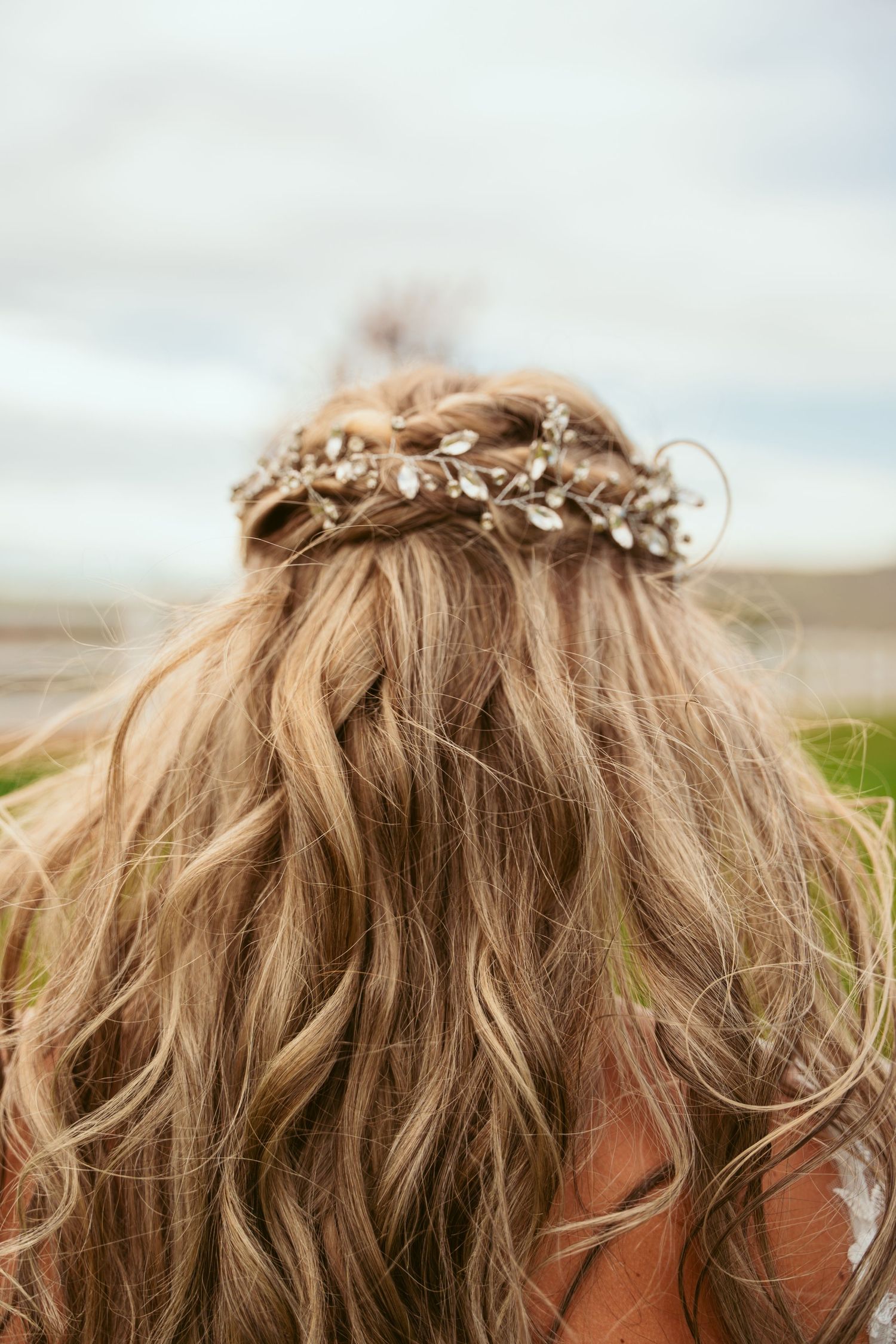 Delicate crystal hairpiece adorns wavy blonde hair against natural outdoor backdrop.