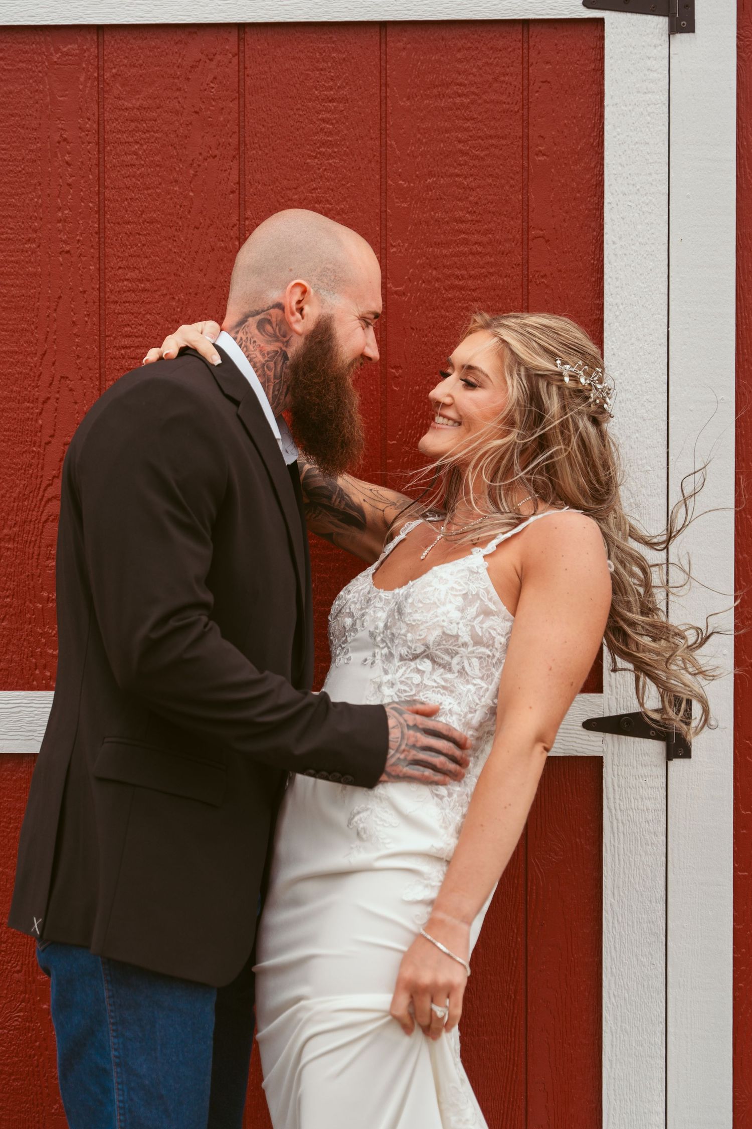 Candid wedding moment captured against bright red barn wall.