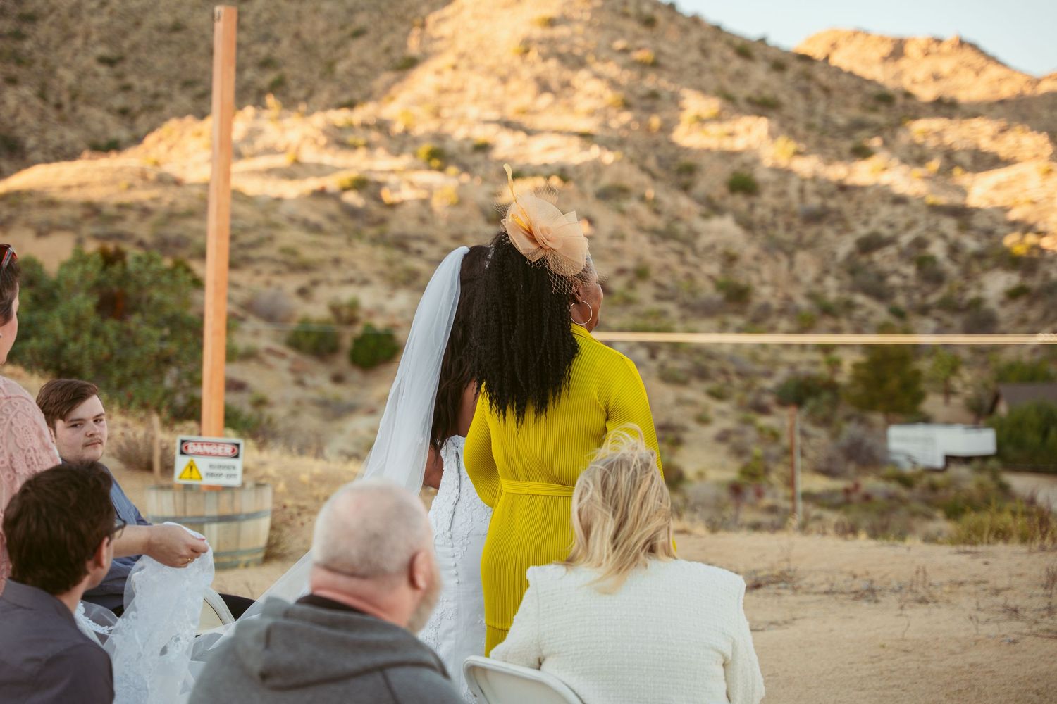 Wedding guests watch ceremony against backdrop of desert mountains at sunset.