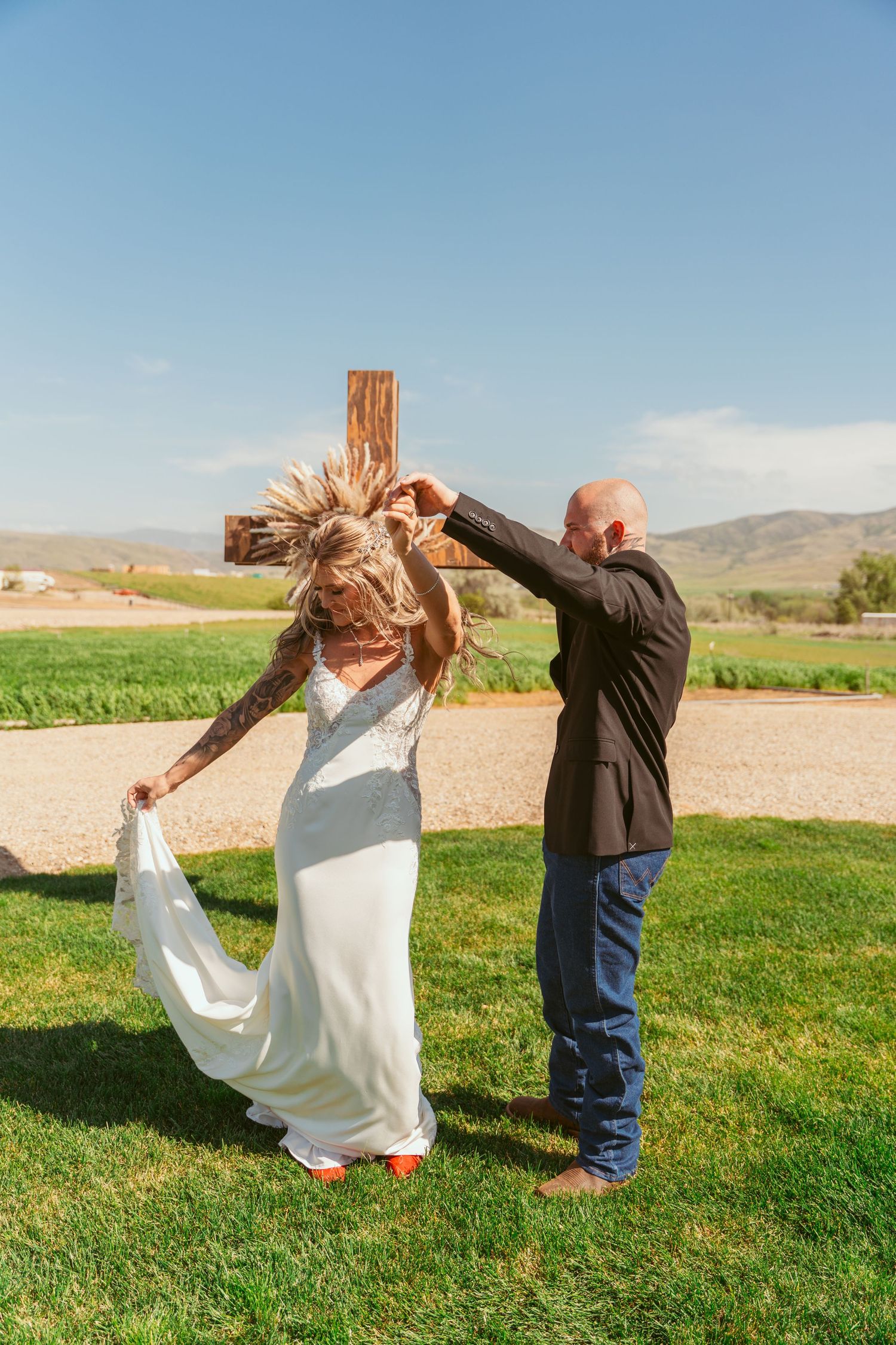 A bride and groom perform a fun dance sequence on green grass with scenic mountain views.