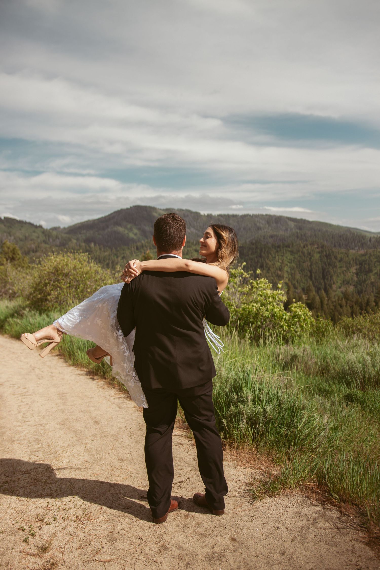A romantic lift pose on a mountain trail with scenic valley views in the background.