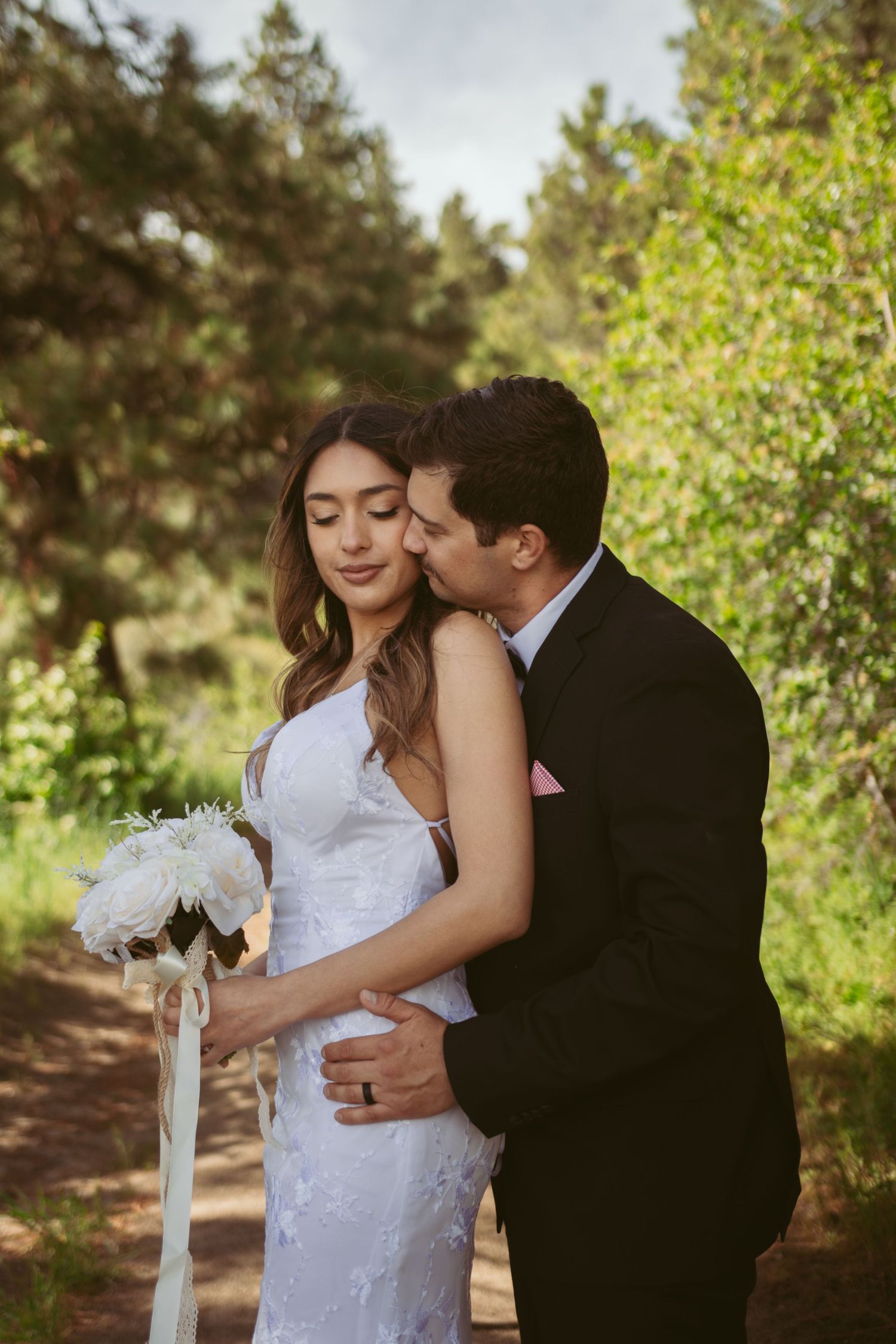 A romantic moment between newlyweds on a forest trail with sunlit foliage.
