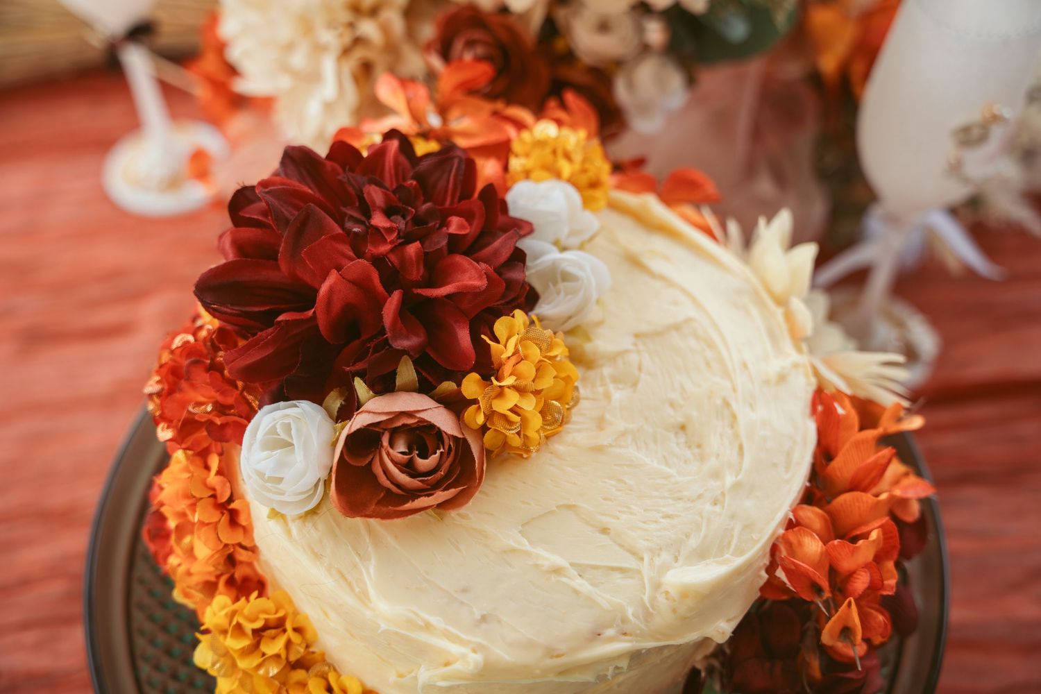 Wedding cake decorated with orange and cream-colored flowers on burgundy tablecloth.