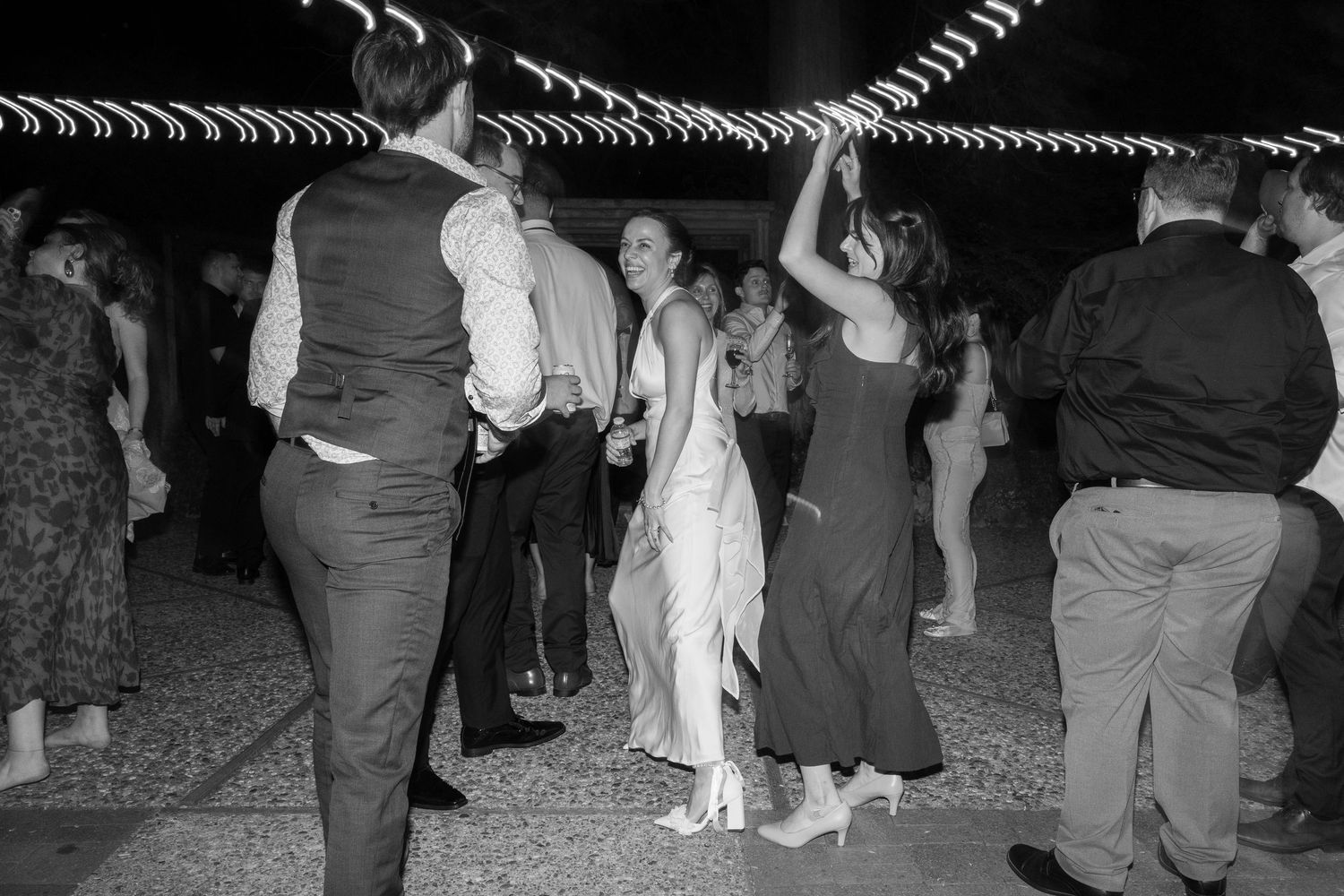 Black and white photo of couples dancing together at a formal event with people watching from the sides.