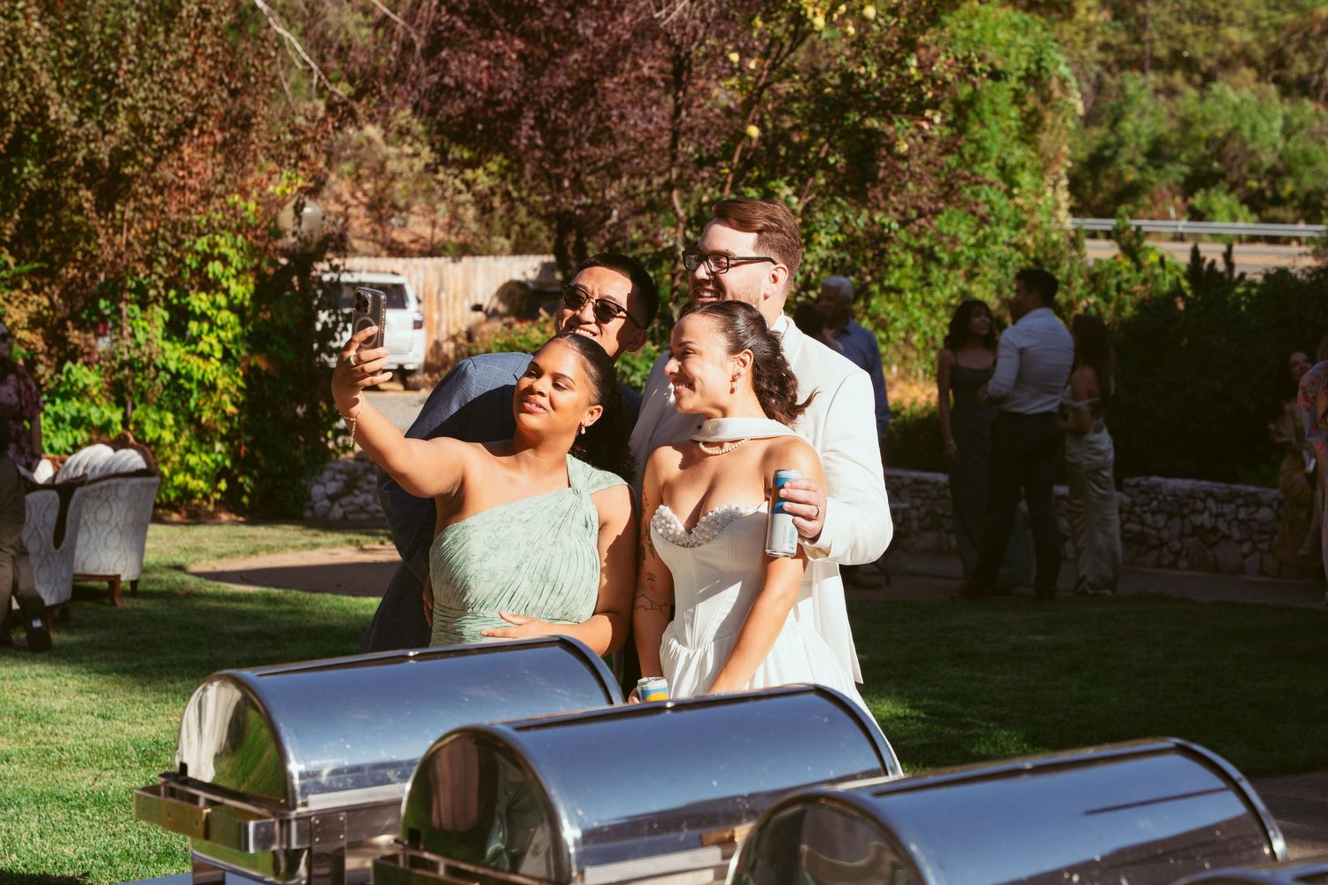 Wedding guests enjoying food at outdoor buffet stations during sunny daytime celebration.