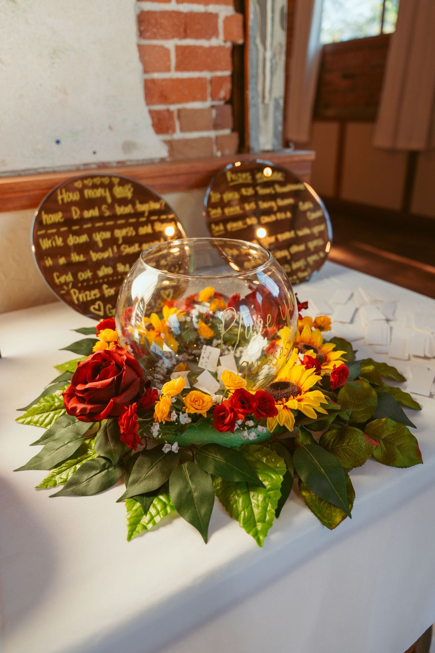 Floral centerpiece with sunflowers and red roses arranged with greenery on a white tablecloth.