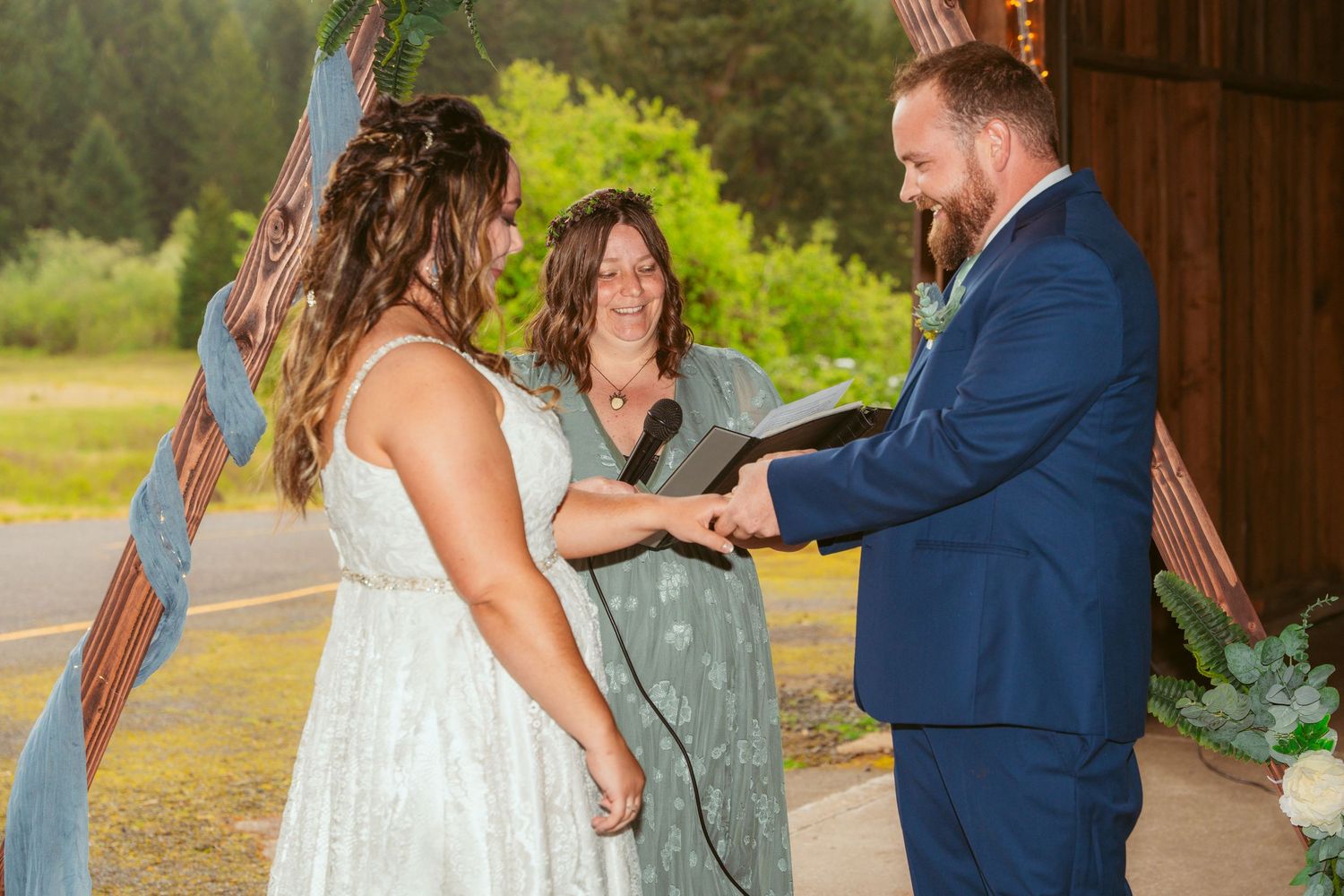 Wedding ceremony inside rustic wooden barn with guests watching couple exchange vows.