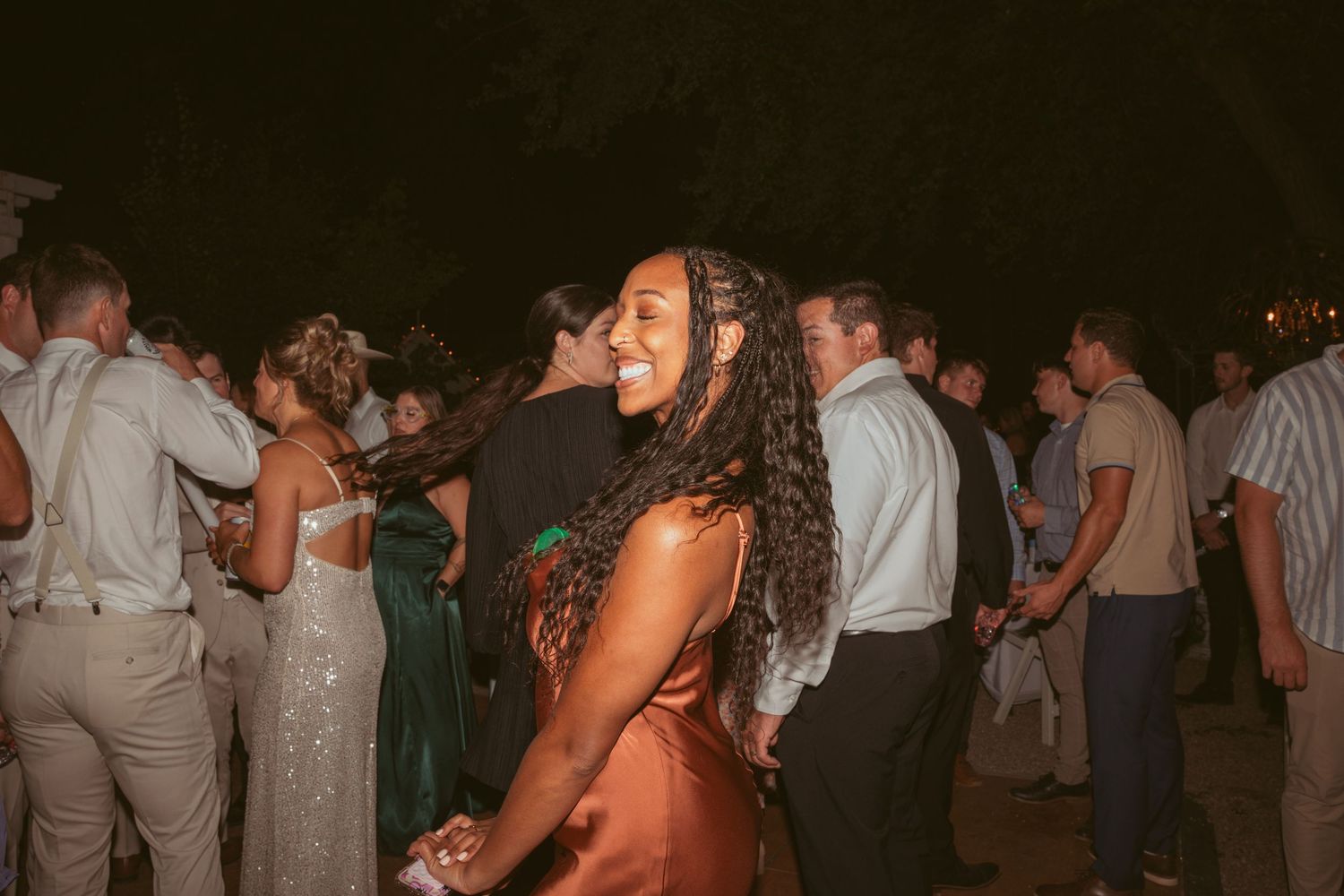 A guest in a rust-colored dress dances enthusiastically at a nighttime wedding reception.