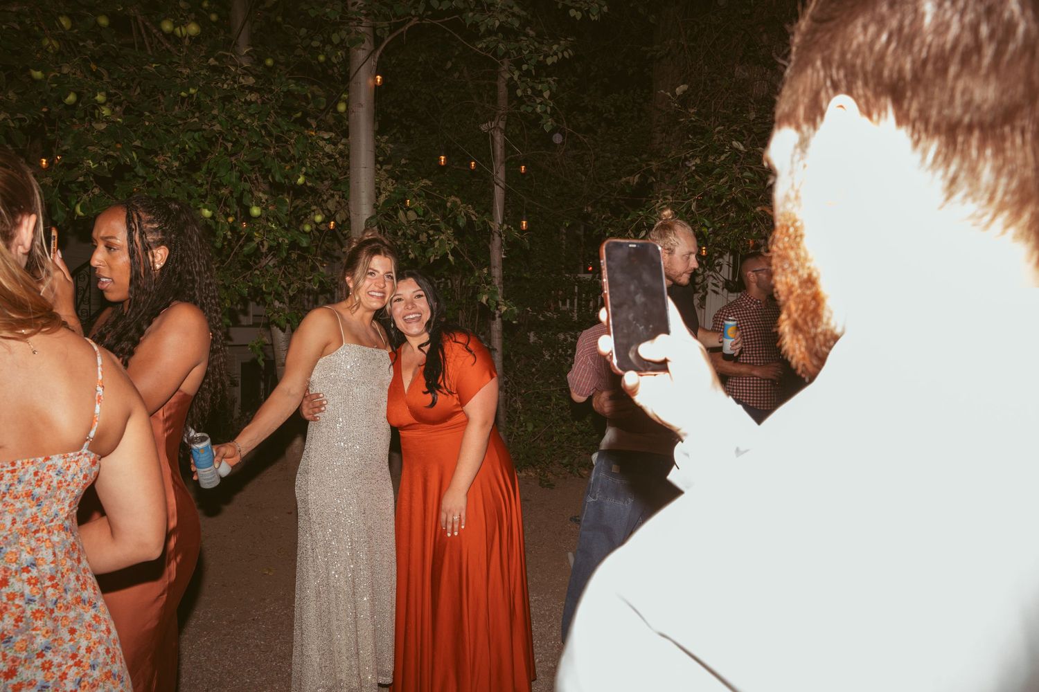 Wedding guests dancing and celebrating on an outdoor dance floor at night with festive lighting.