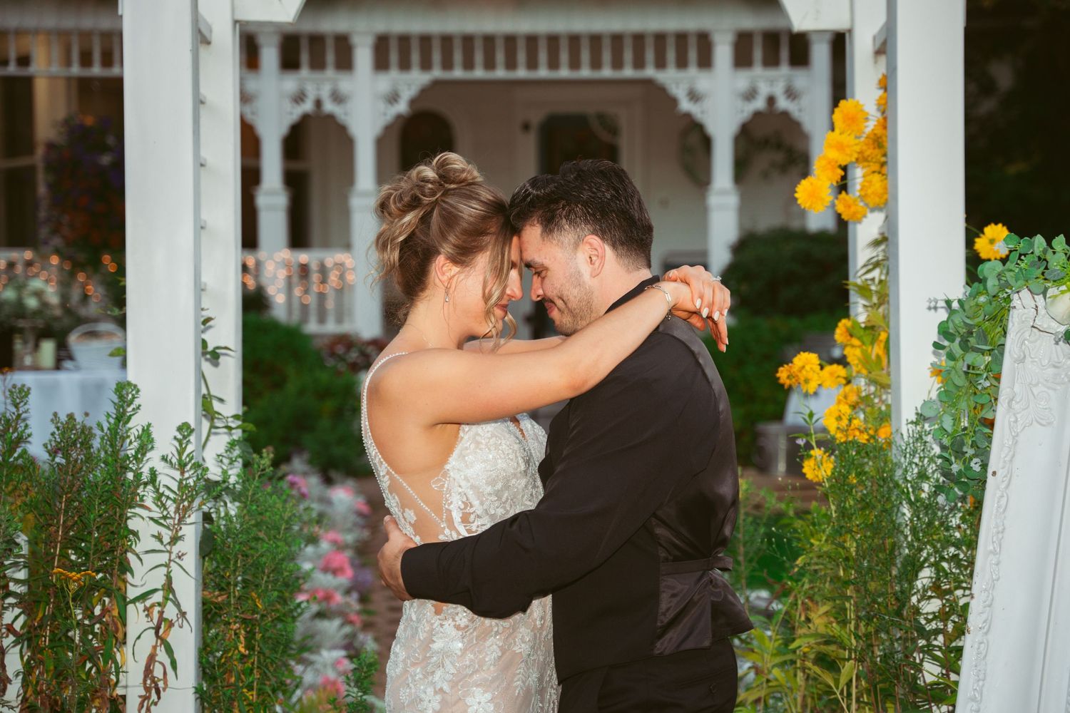 Couple dances intimately near white gazebo with sunflowers in background.