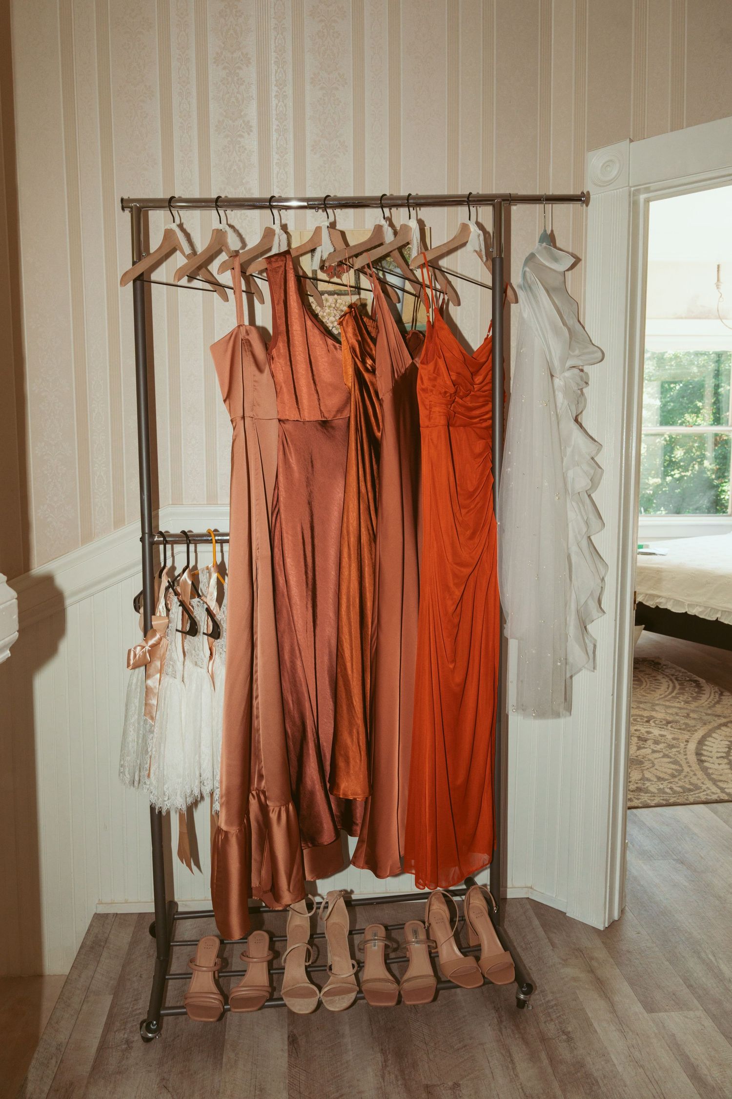 Coral and peach colored bridesmaid dresses hanging on a clothing rack with matching shoes below.
