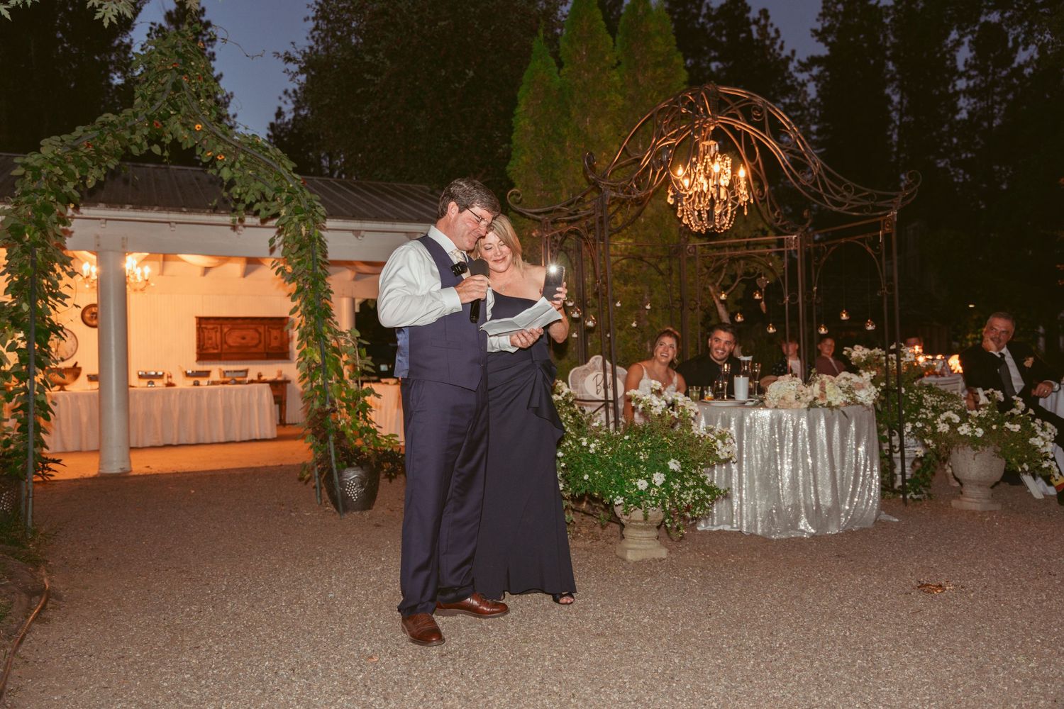 Couple dancing at an outdoor evening reception with decorated garden setting.