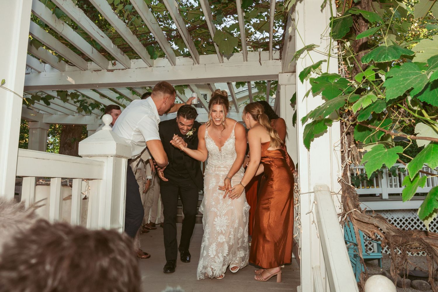 Wedding party making their grand entrance under a white pergola decorated with greenery.