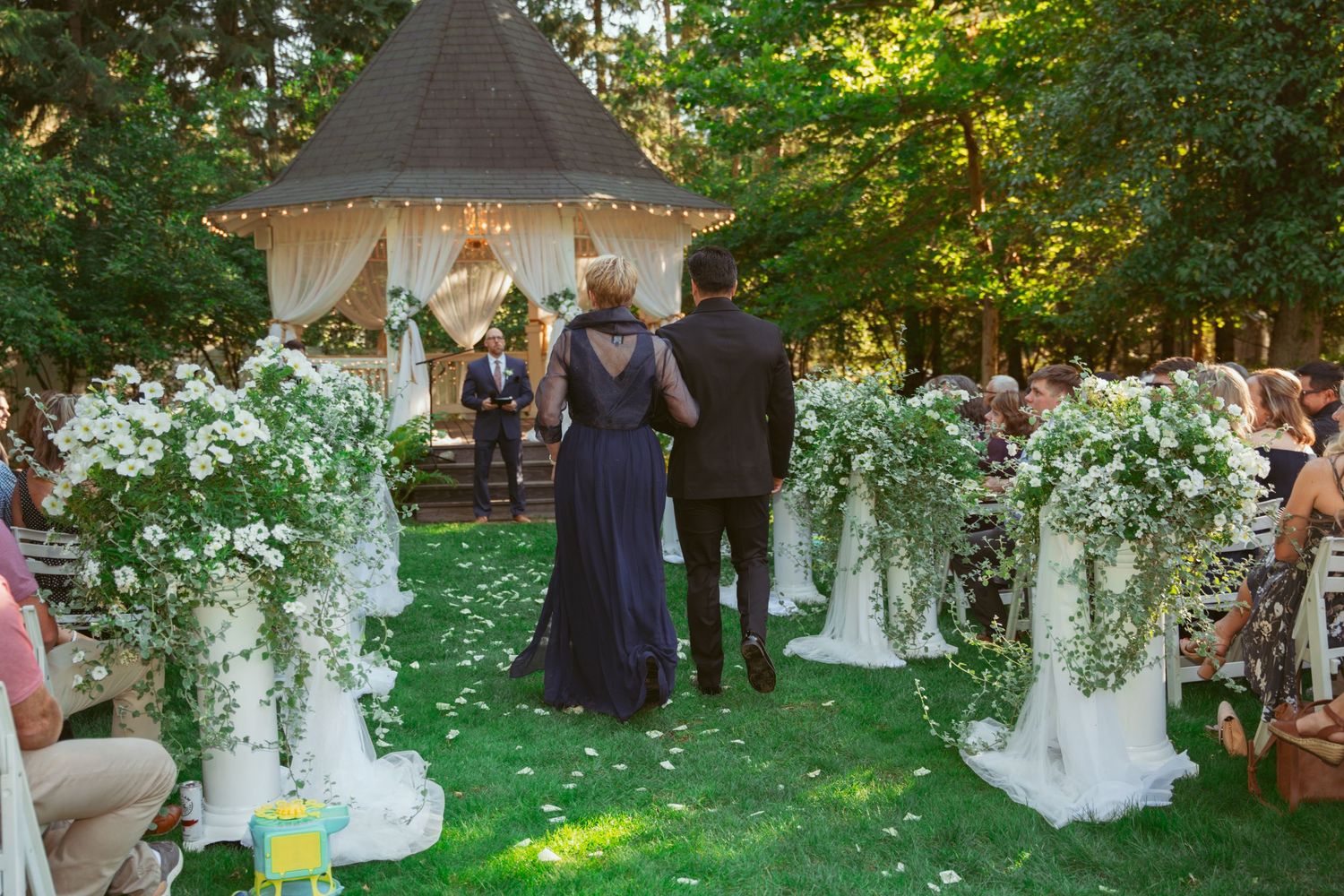 Wedding guests gather under elegant outdoor tent decorations with hanging floral arrangements and string lights at dusk.