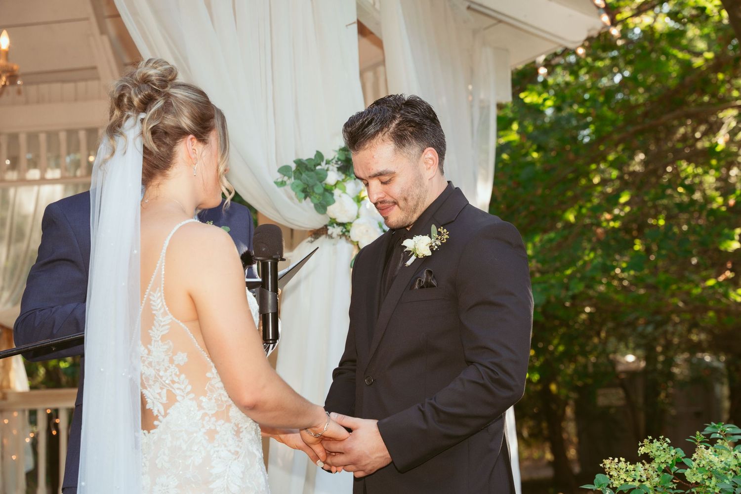 A couple shares a tender moment during their wedding ceremony on a sunny porch surrounded by greenery.